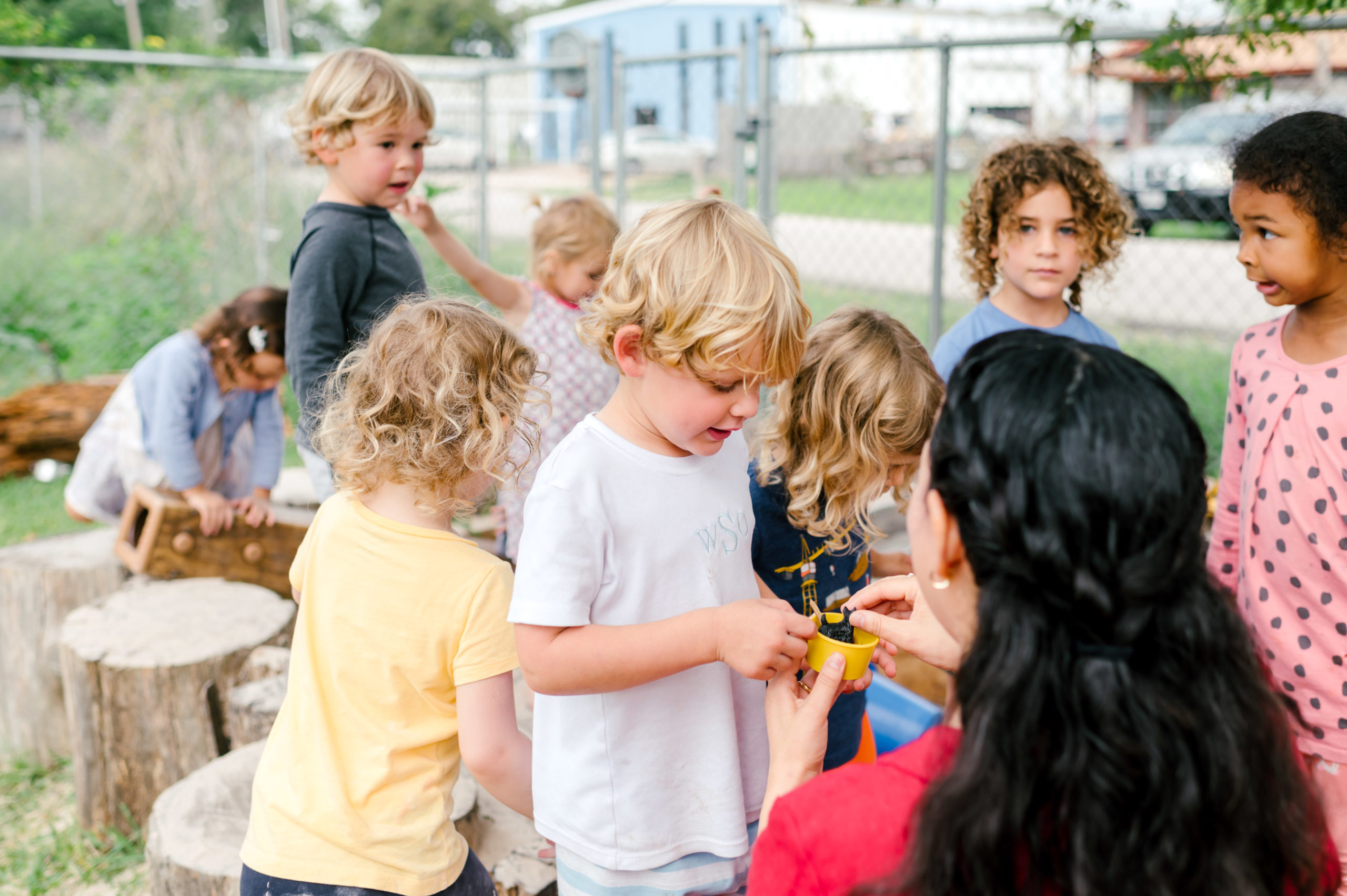 Photo of woman child development coach in a beautiful red dress interacting with kids on a playground outside  during her branding photography session
