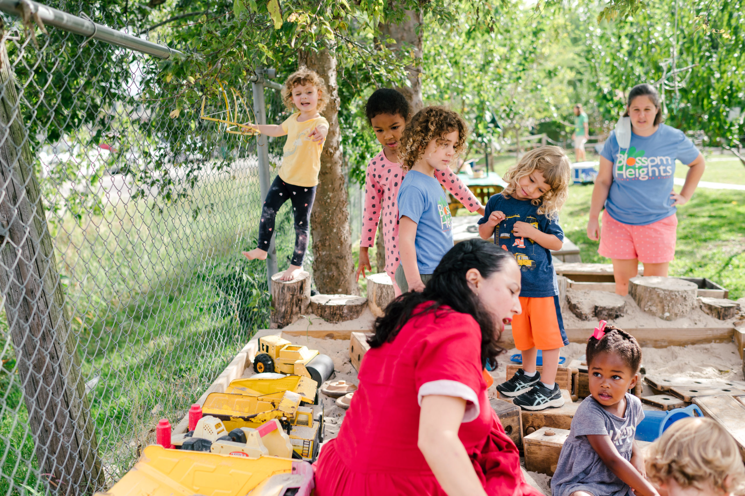 Photo of woman child development coach in a beautiful red dress interacting with kids on a playground outside during her branding photography session
