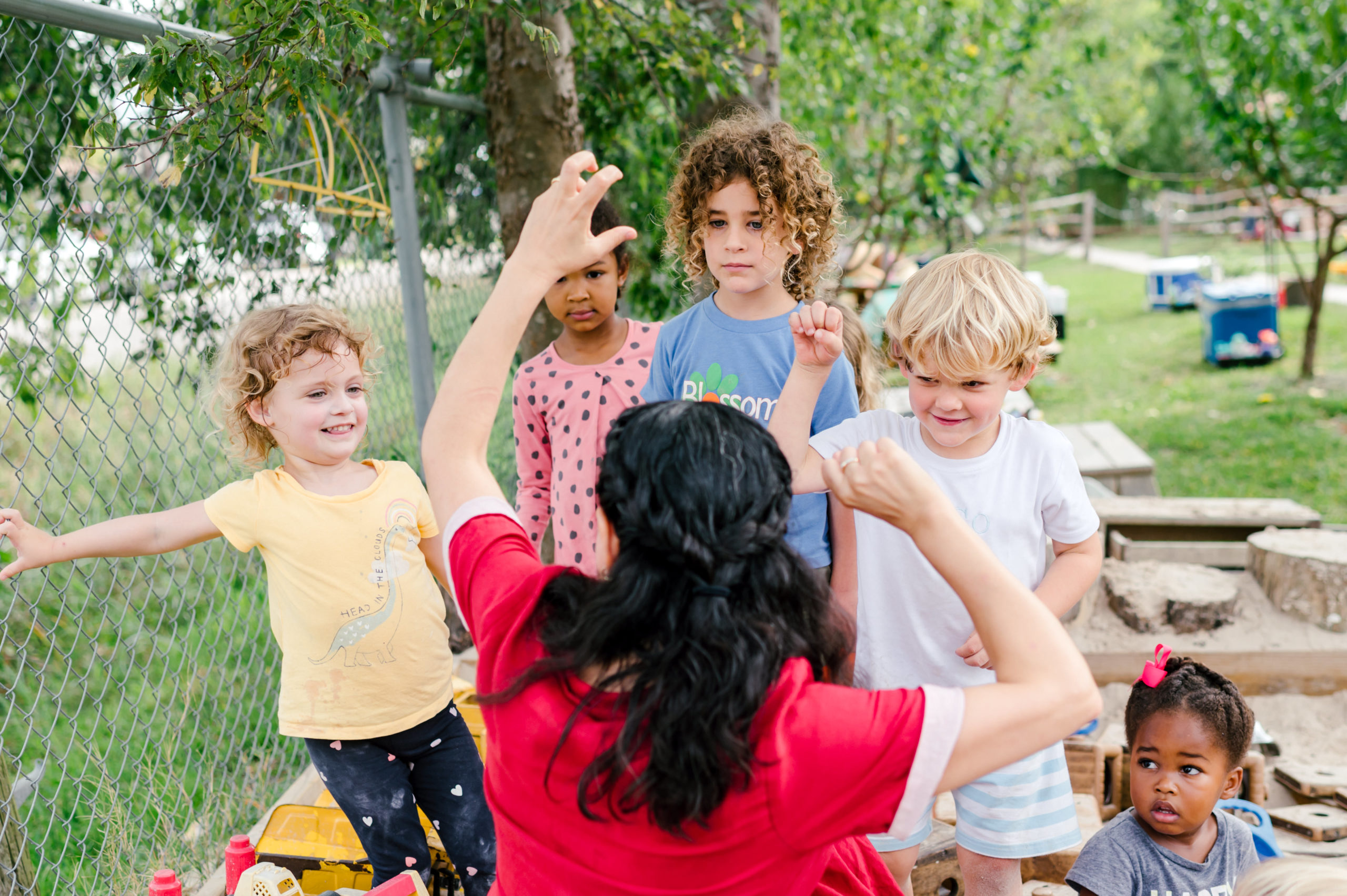 Photo of woman child development coach in a beautiful red dress interacting with kids on a playground outside during her branding photography session
