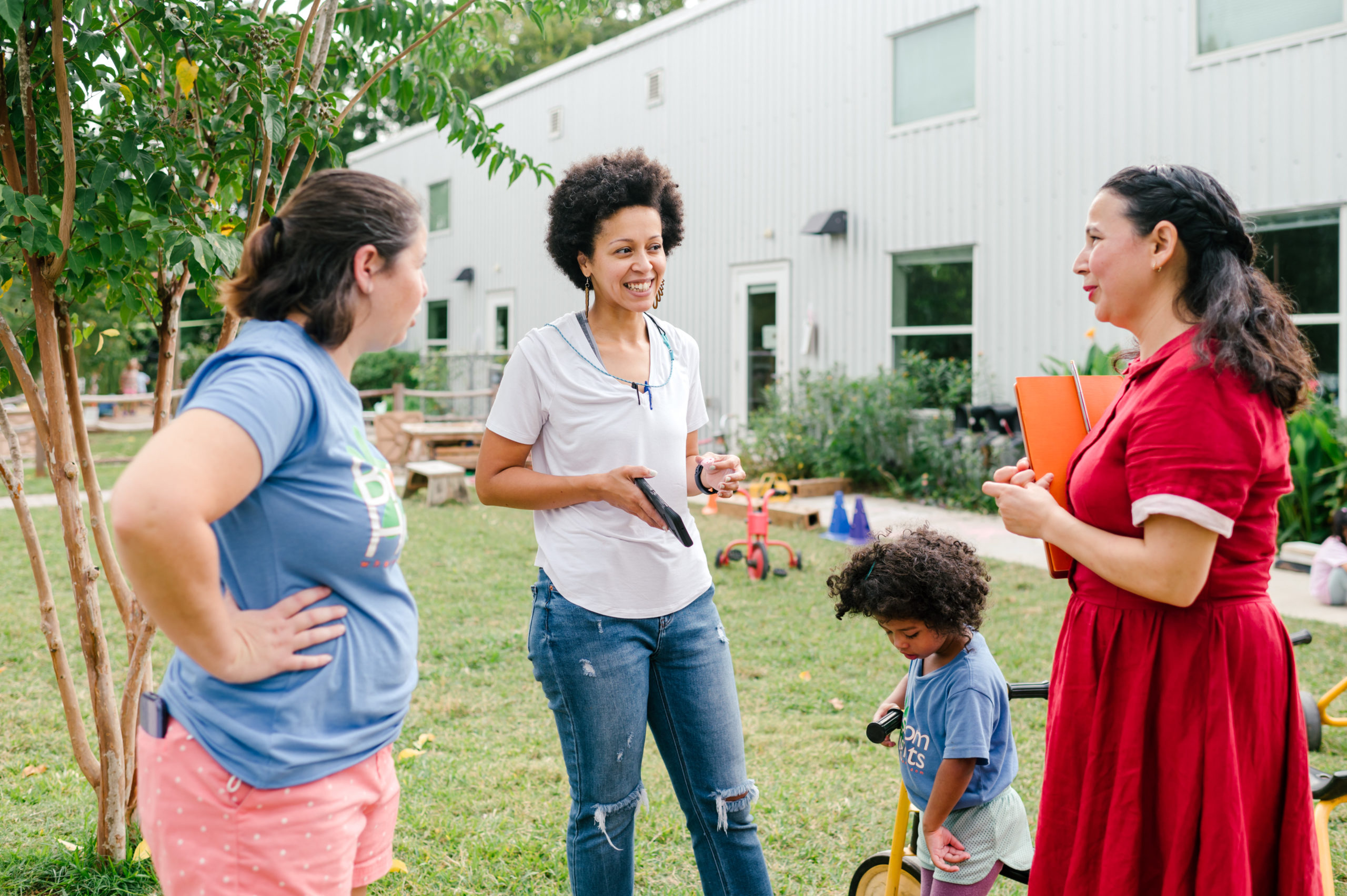 Photo of woman child development coach in a beautiful red dress interacting with other teachers and coaches outside
