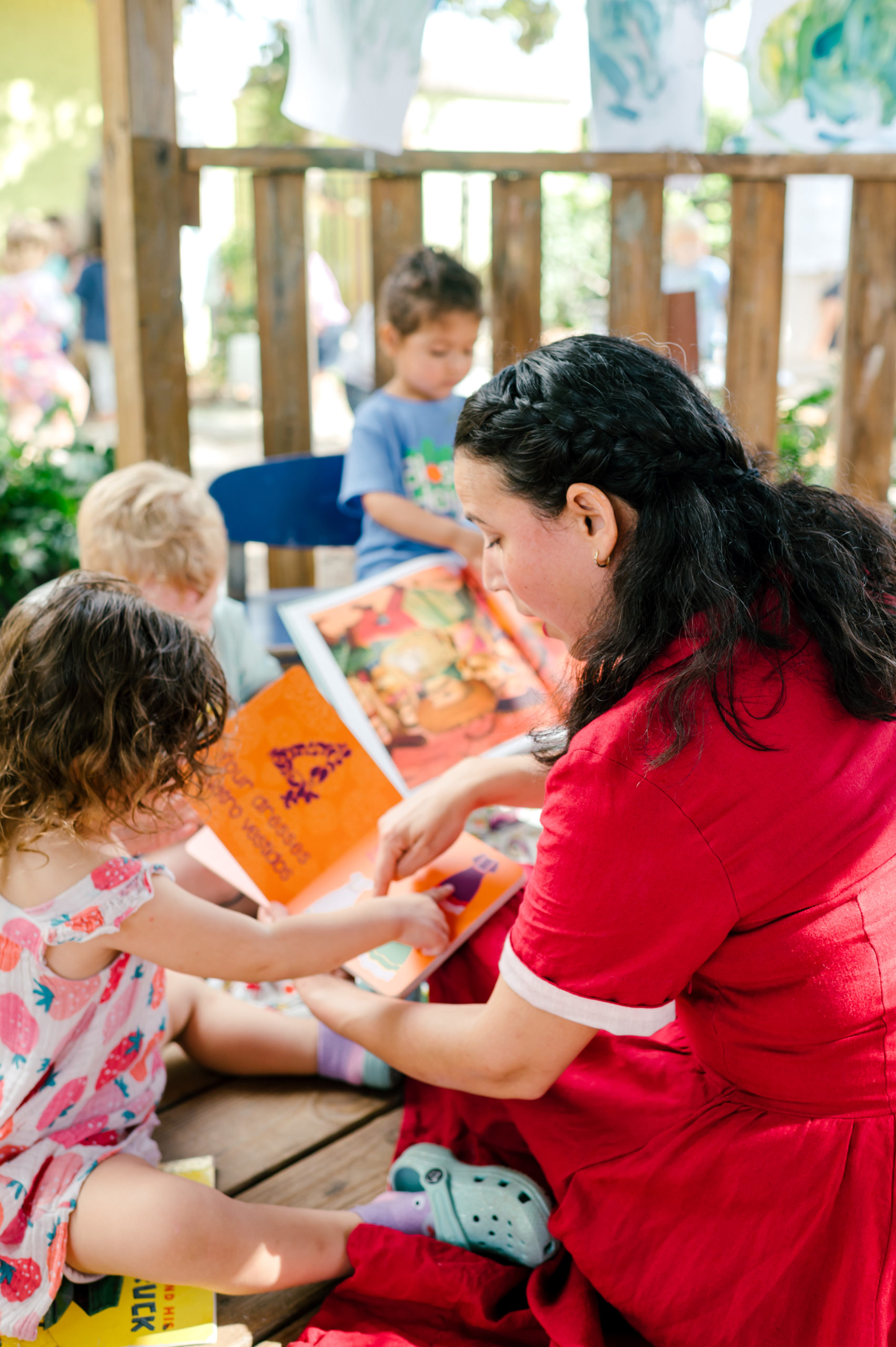 Photo of woman child development coach in a beautiful red dress interacting with kids on a playground outside during her branding photography session
