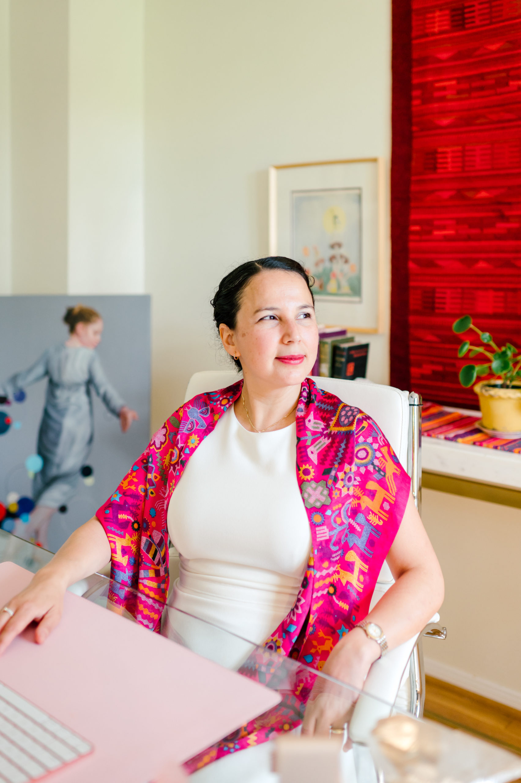 Photo of woman child development coach in a white dress and colorful pink scarf sitting at her desk in her at home office during her branding photography session