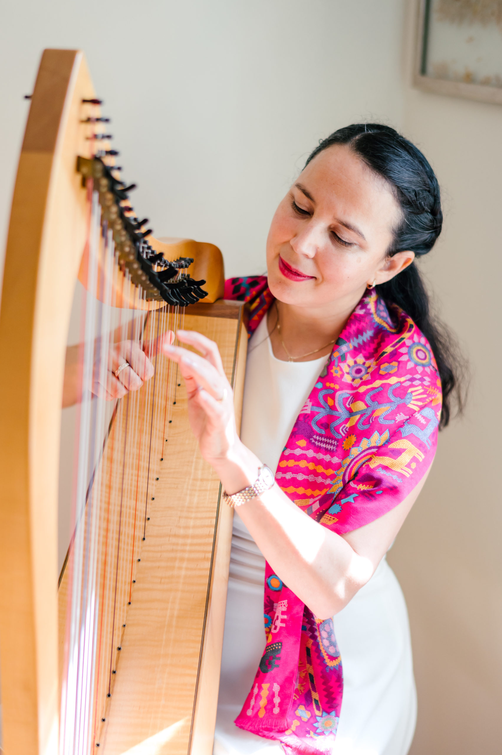 Photo of woman child development coach in a white dress and colorful pink scarf playing a harp at home  during her branding photography session 