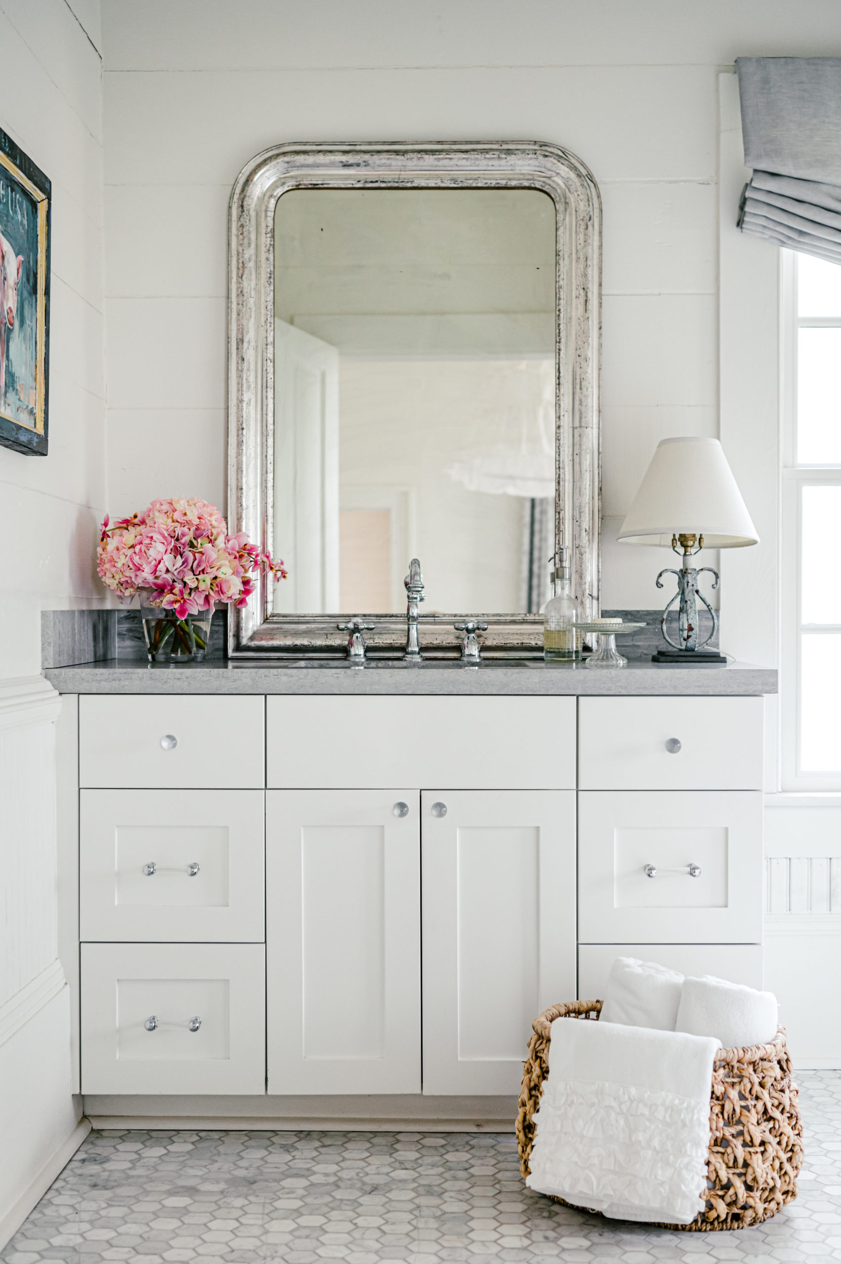 Interior Photography of a beautiful bathroom and sink with white cabinets and gray sink with a tall mirror and pink flowers 