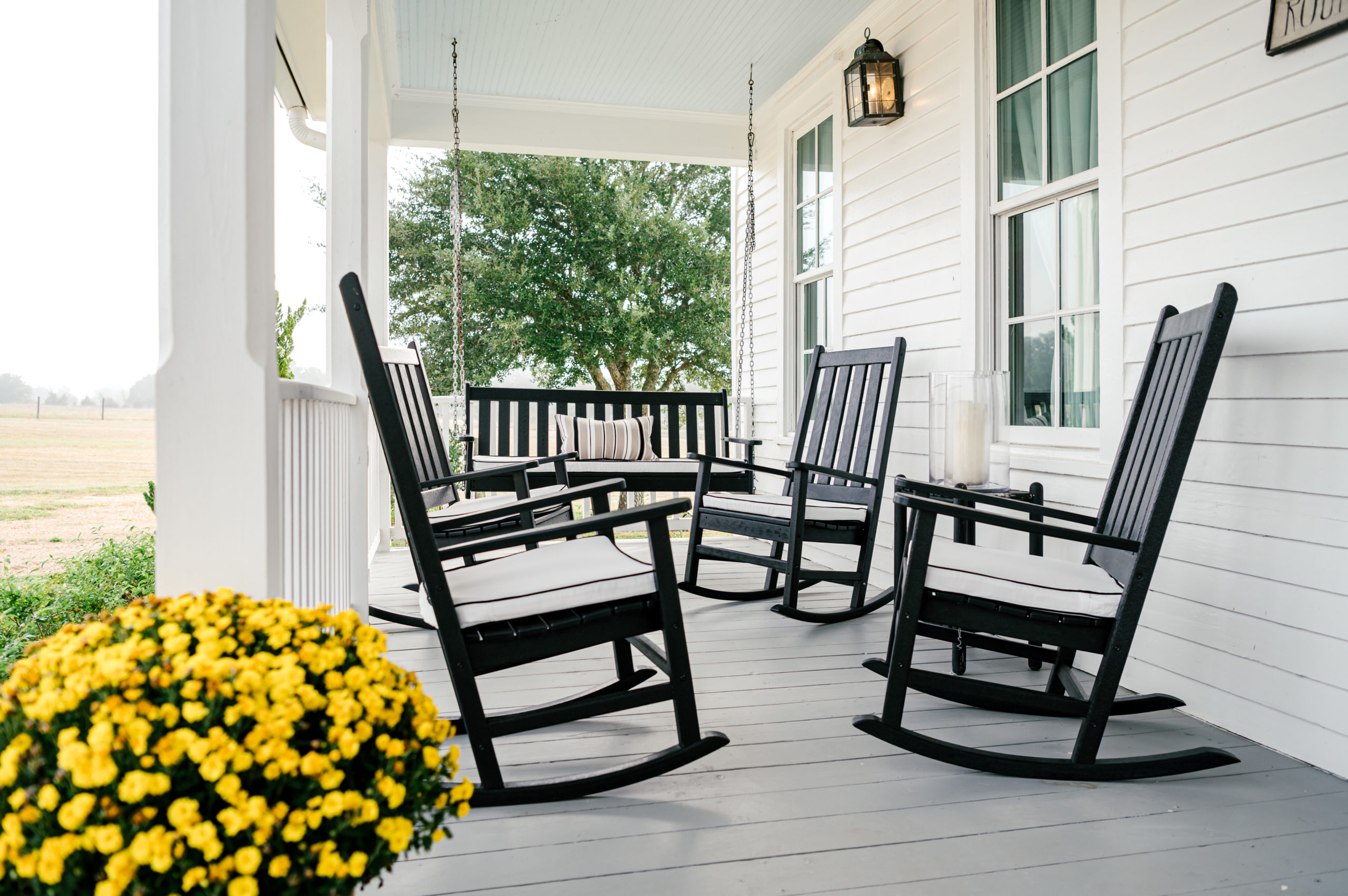 Photo of black rocking chairs on a beautiful farmhouse porch with yellow flowers