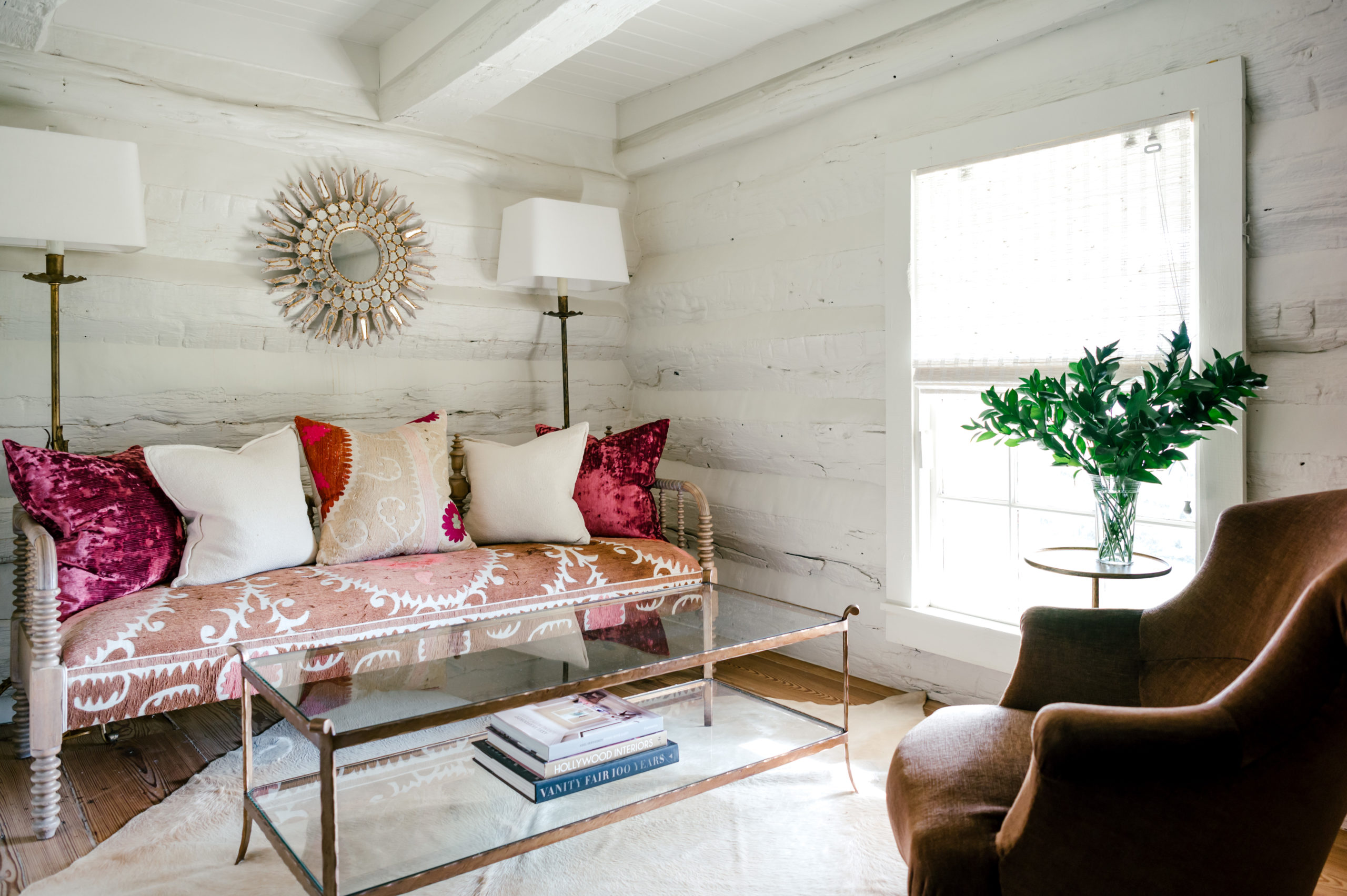 Photo of lounge area with a unique pink couch with white and pink pillows sitting on top as well as a glass table and brown lounge chair