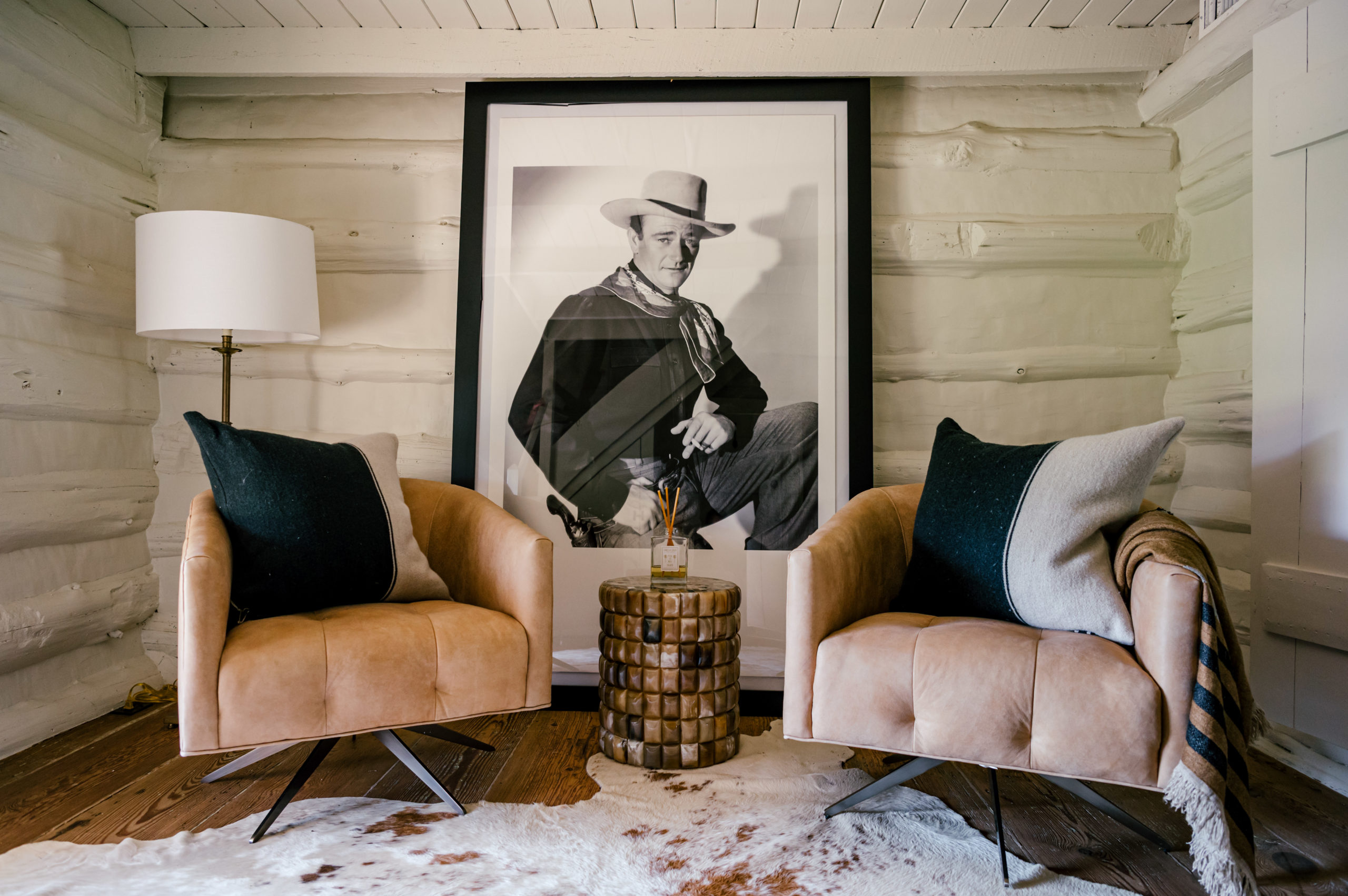 Photo of lounge area with lounge chairs with black and grey pillows sitting on top of a cow skin carpet and a western picture frame laying on the wall