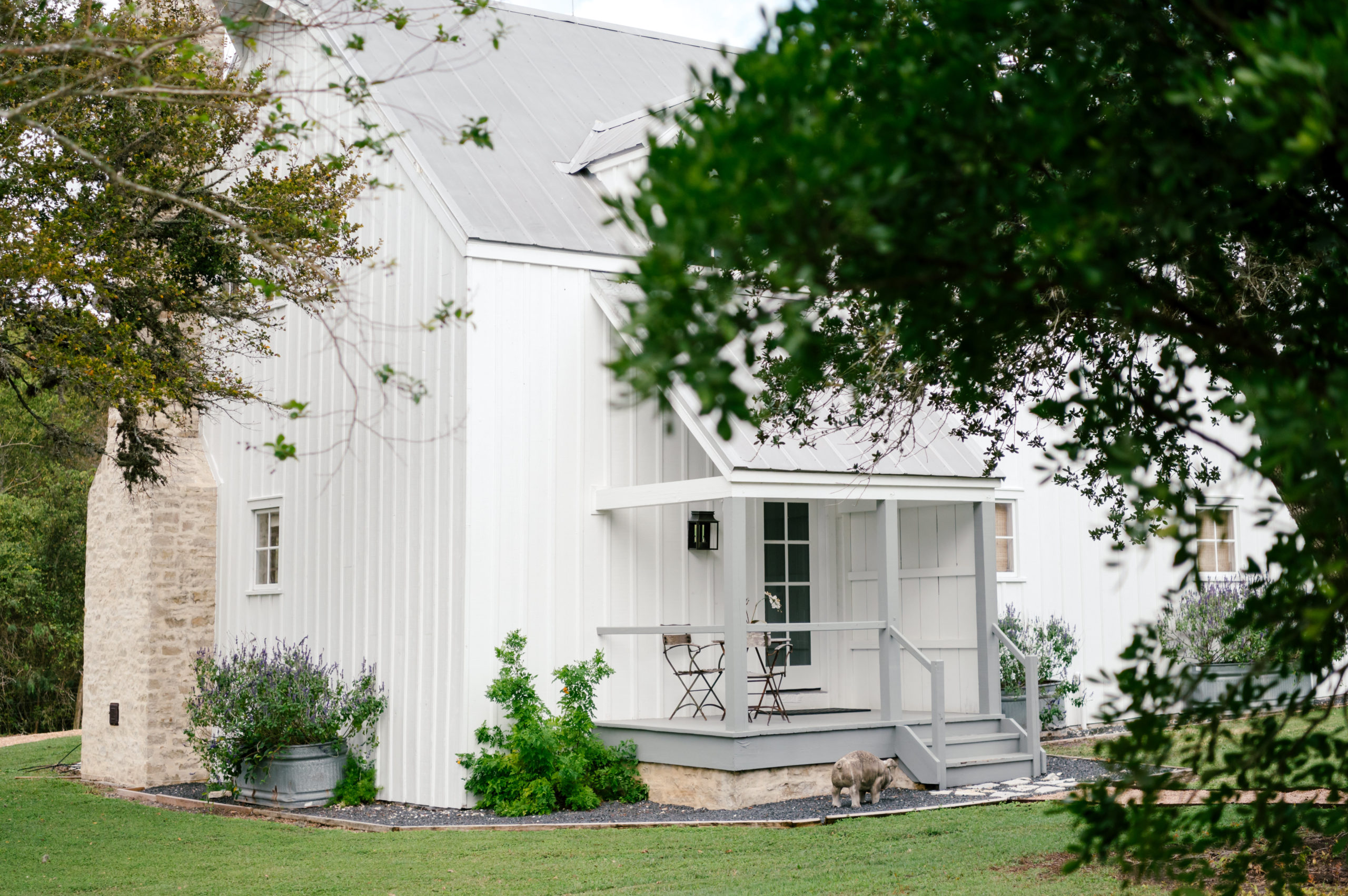 Photo of a beautiful farmhouse white porch with table and chairs as well as a cement pig standing in the gravel