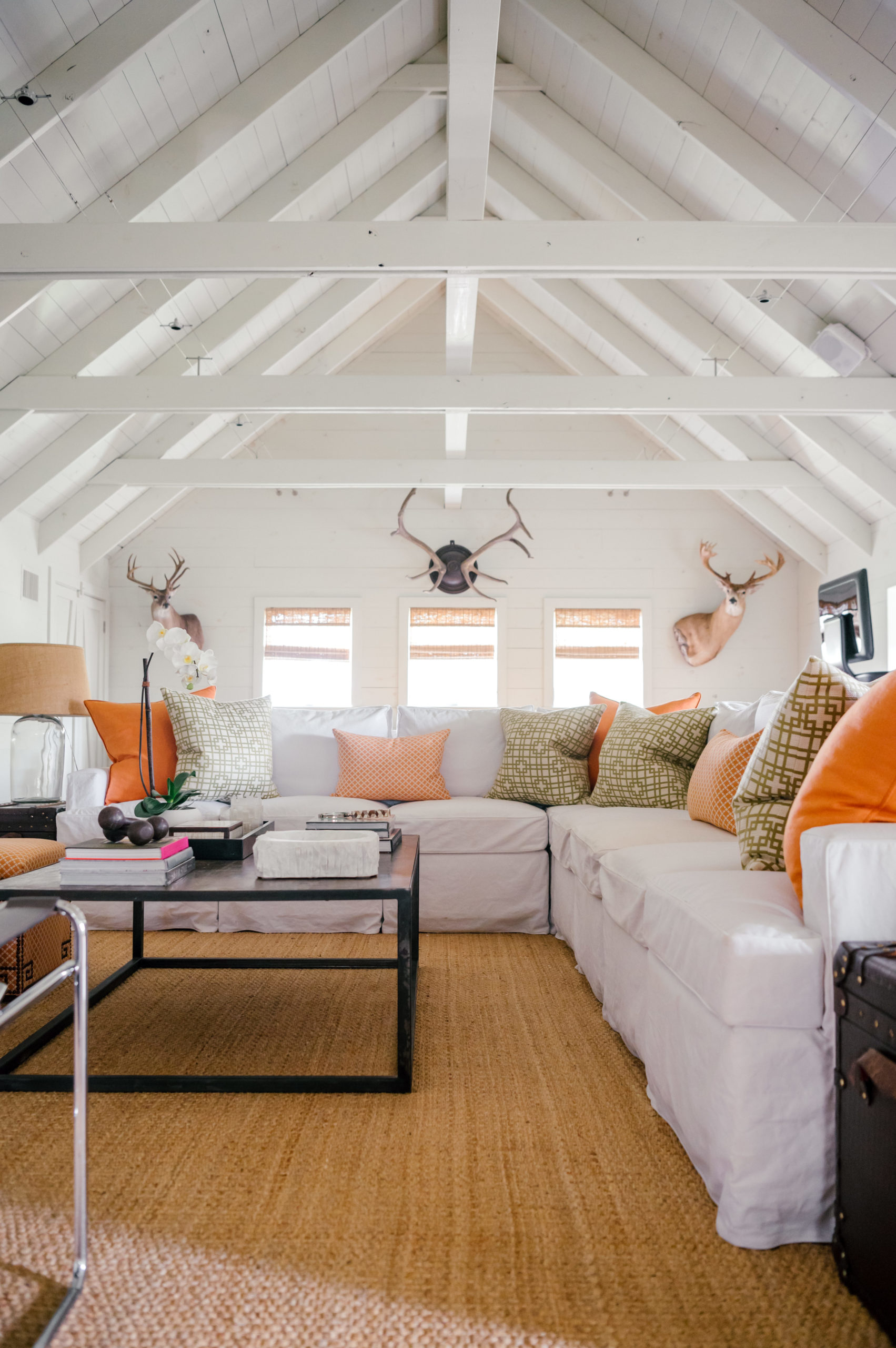 Interior Photography of white sectional couch with multi-color orange pillows and deer heads and antlers hanging on the wall