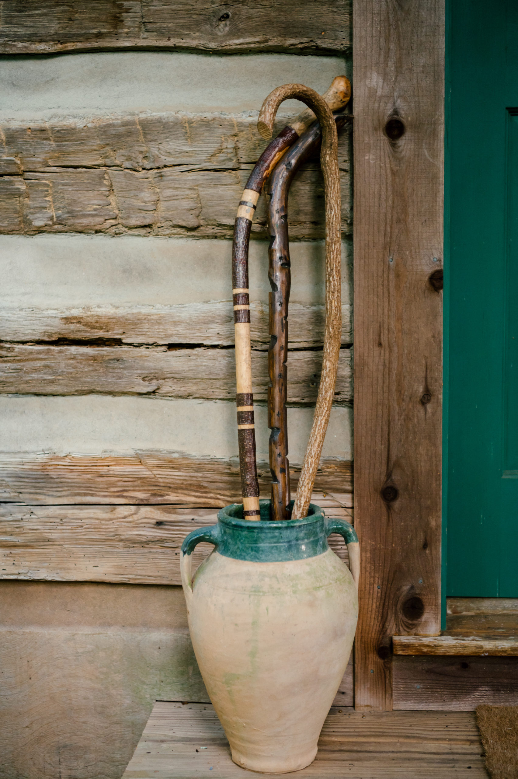 Photo of wooden handle umbrellas in a tall standing tan pot on the front porch of a wood cabin