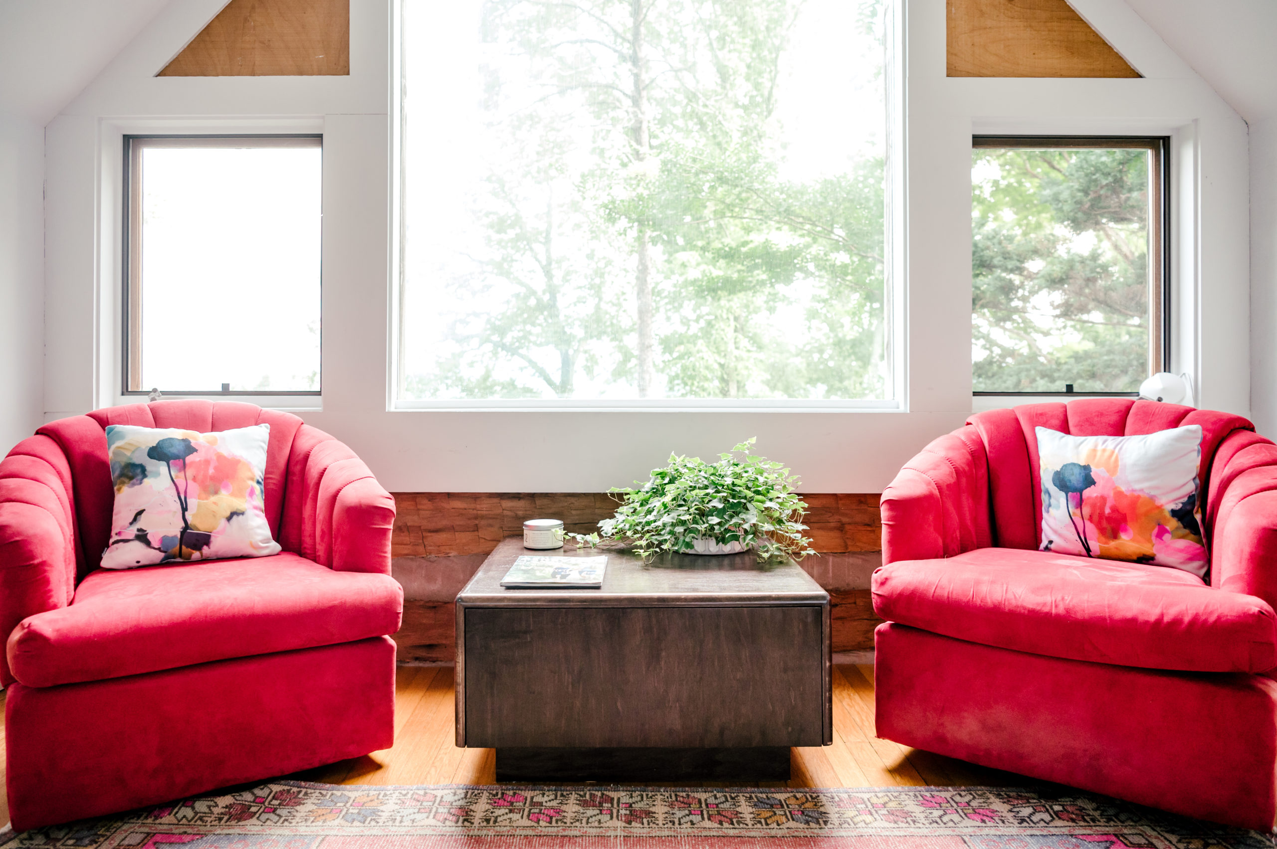 Photo of living room interior furniture, with a wooden table between two red love seats with pillows sitting on them