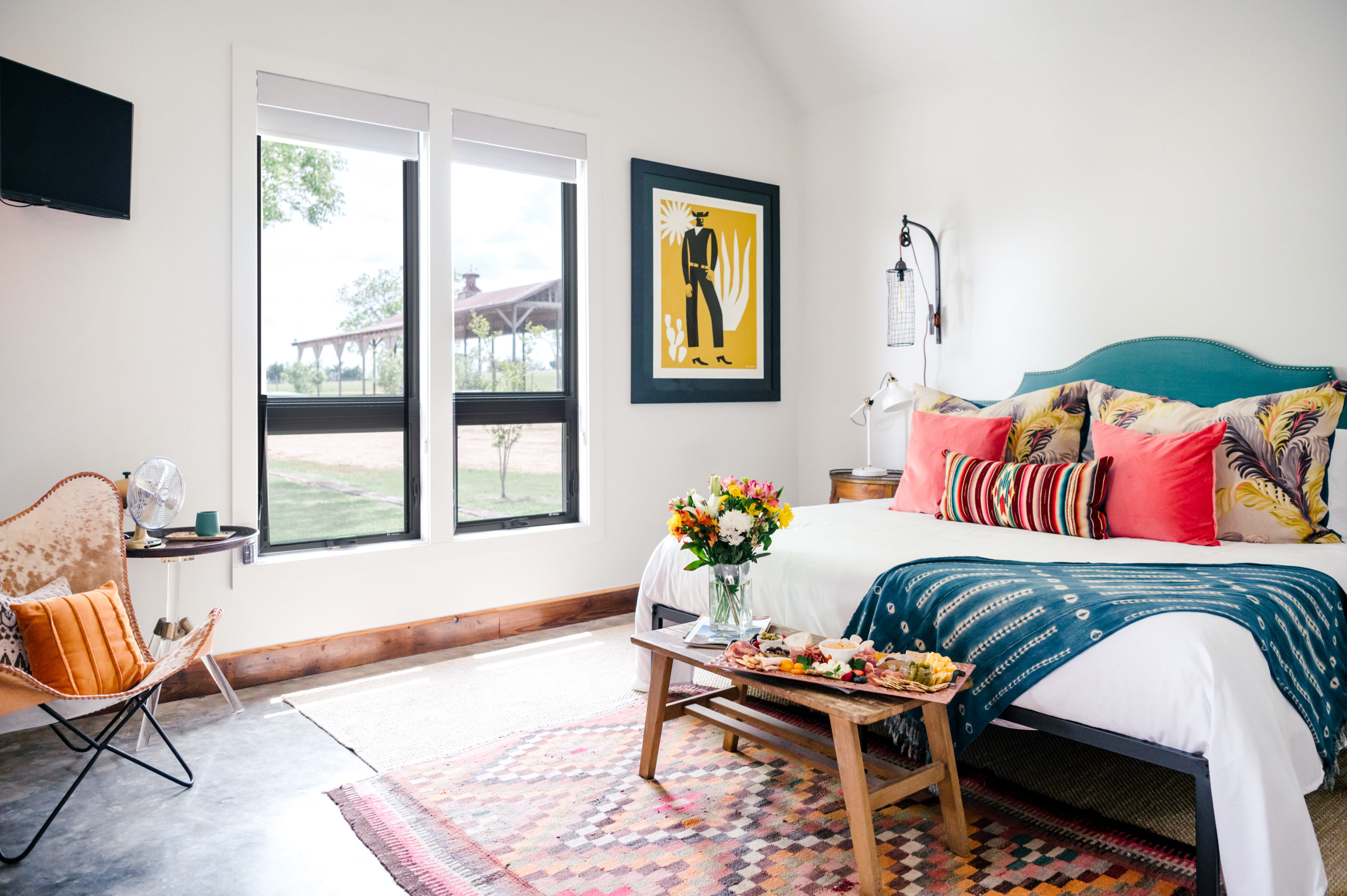 Room with a queen sized bed with colorful pillows and western art hanging on the wall