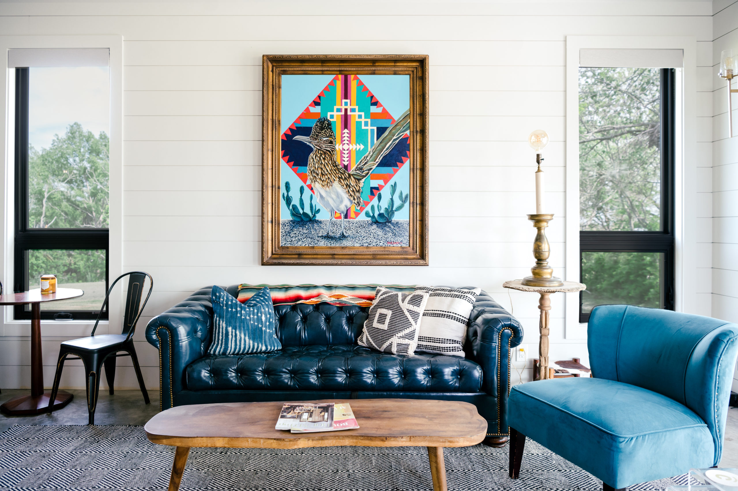 Well lit room with blue leather couch, blue velvet love seat and western art hanging on the wall