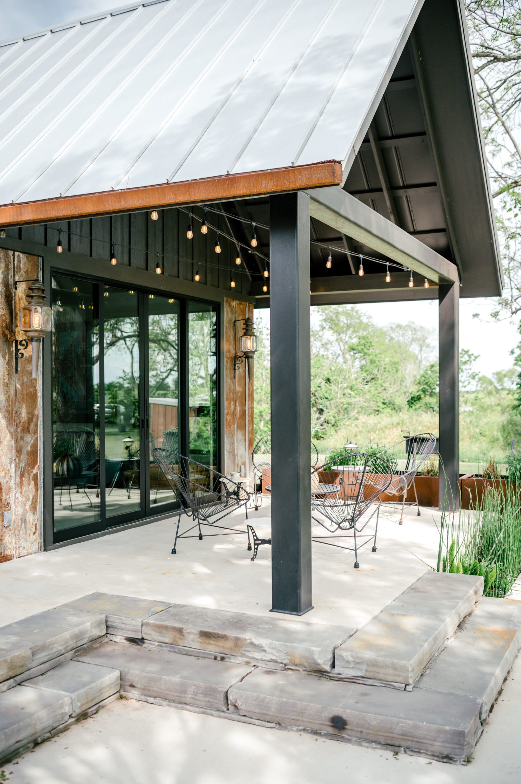 Airbnb exterior with dark exterior paint mixed with wood and rusted-looking metal and metal outdoor lounge furniture 