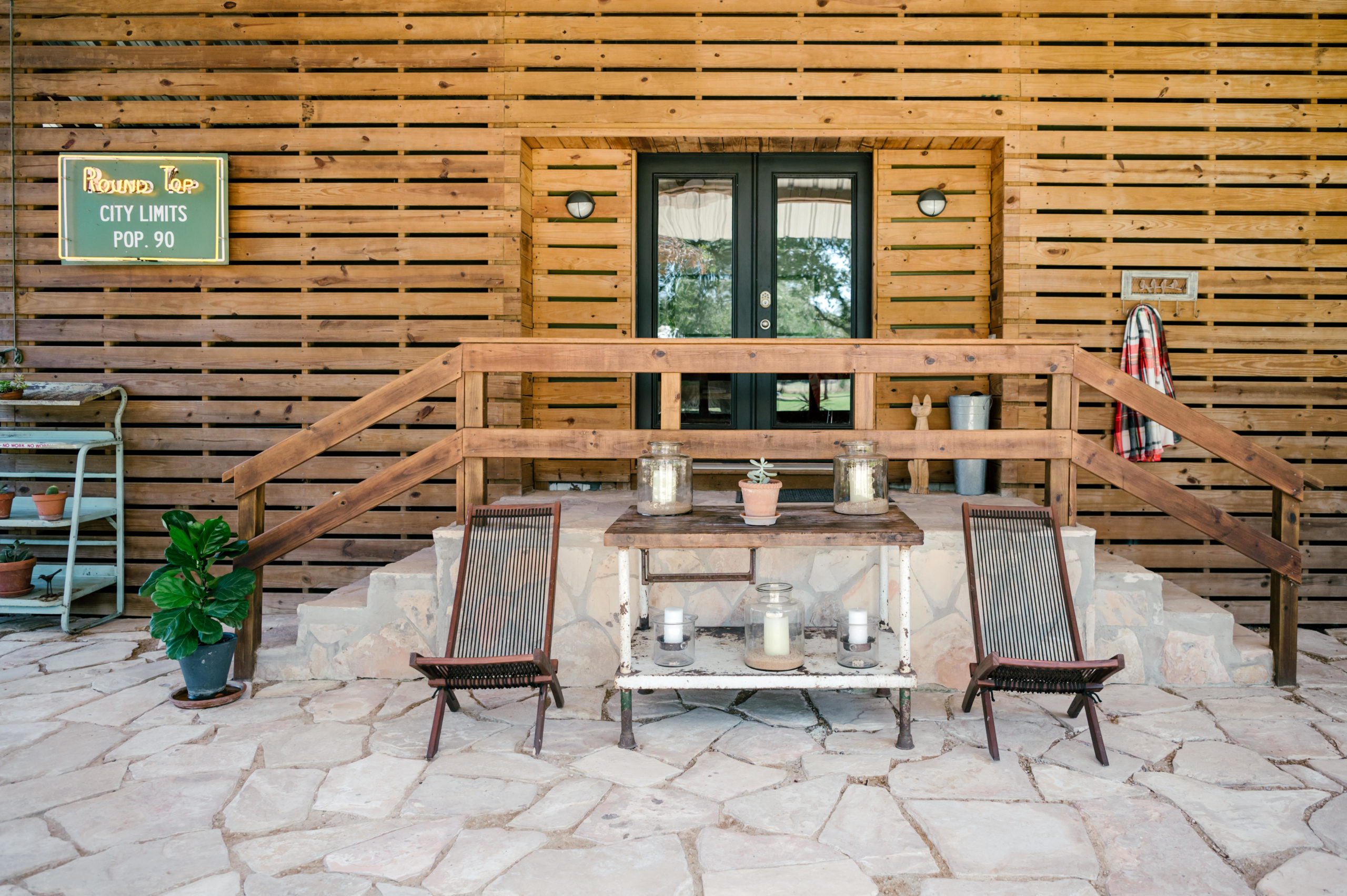 Outdoor lounge furniture and rustic plant table sitting in front of the wooden exterior of an airbnb