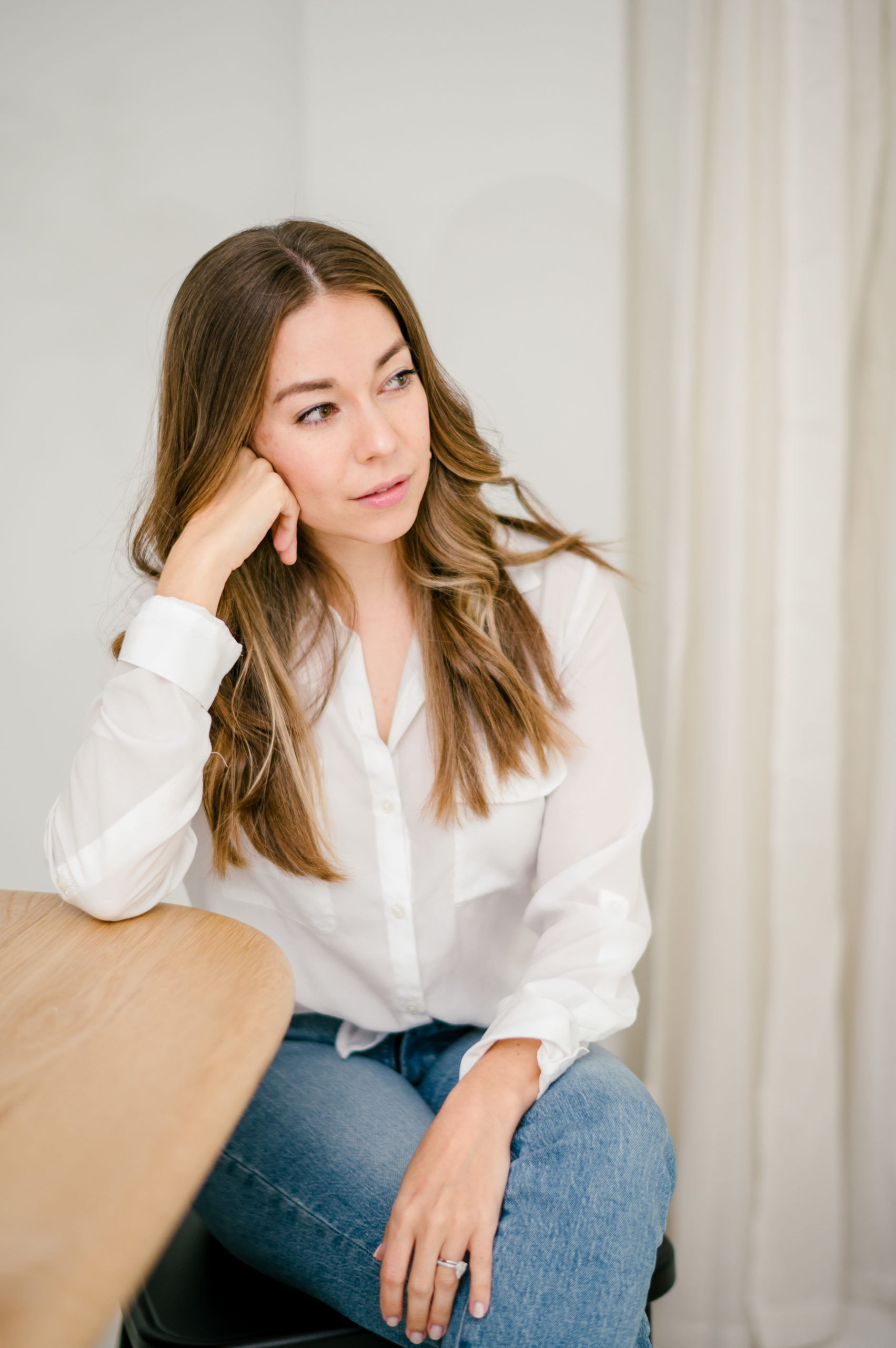 Woman in a white button up and jeans leaning on a wooden table