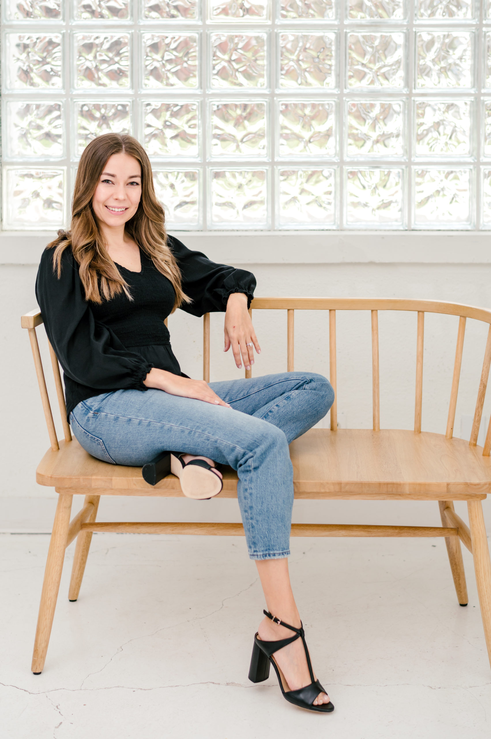 Woman sitting on wooden bench smiling in a white blouse and jeans for her brand photography photos