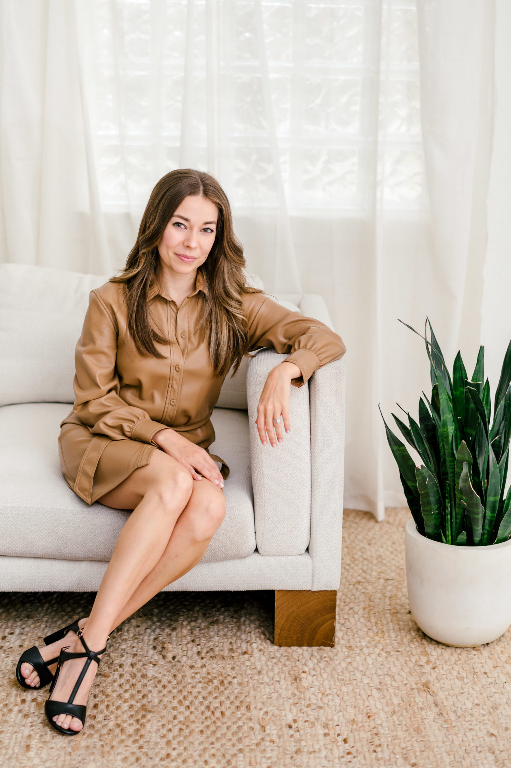 Woman in a leather dress sitting on a couch criss cross for her brand photography photos