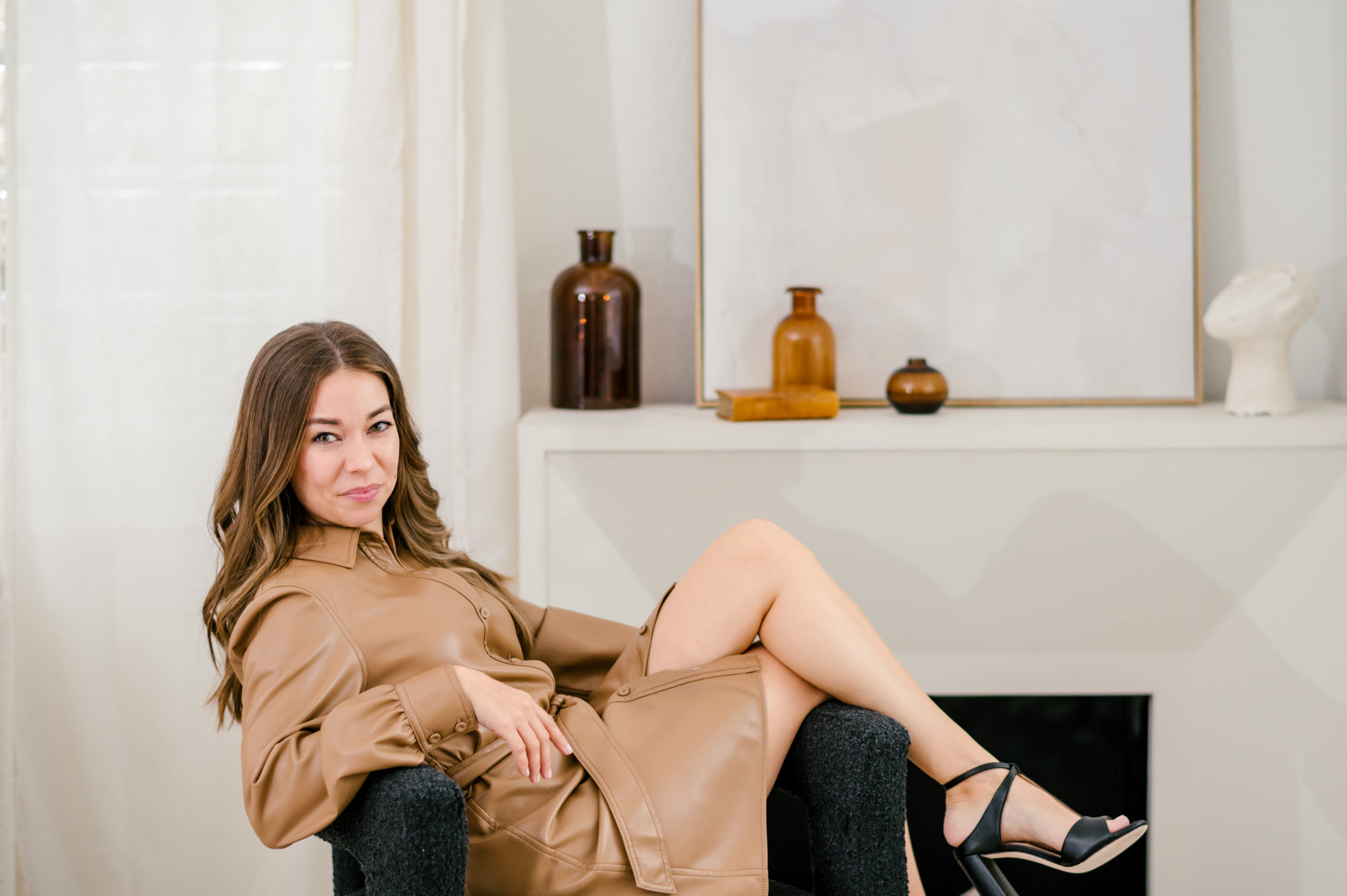 Woman sitting on black love seat in a brown leather dress posing