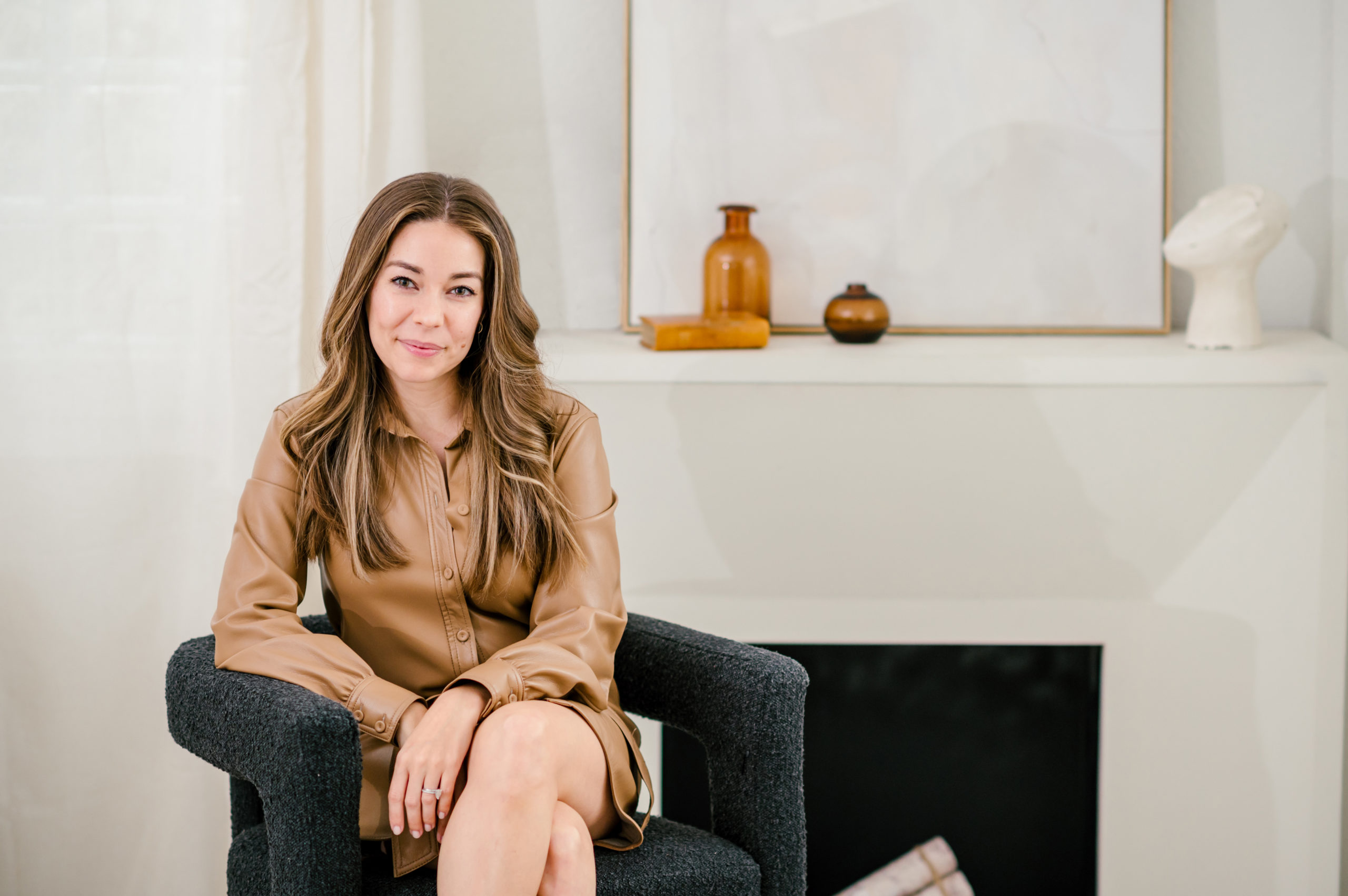 Woman sitting on a black loveseat in a brown dress jacket dress for her brand photography photos