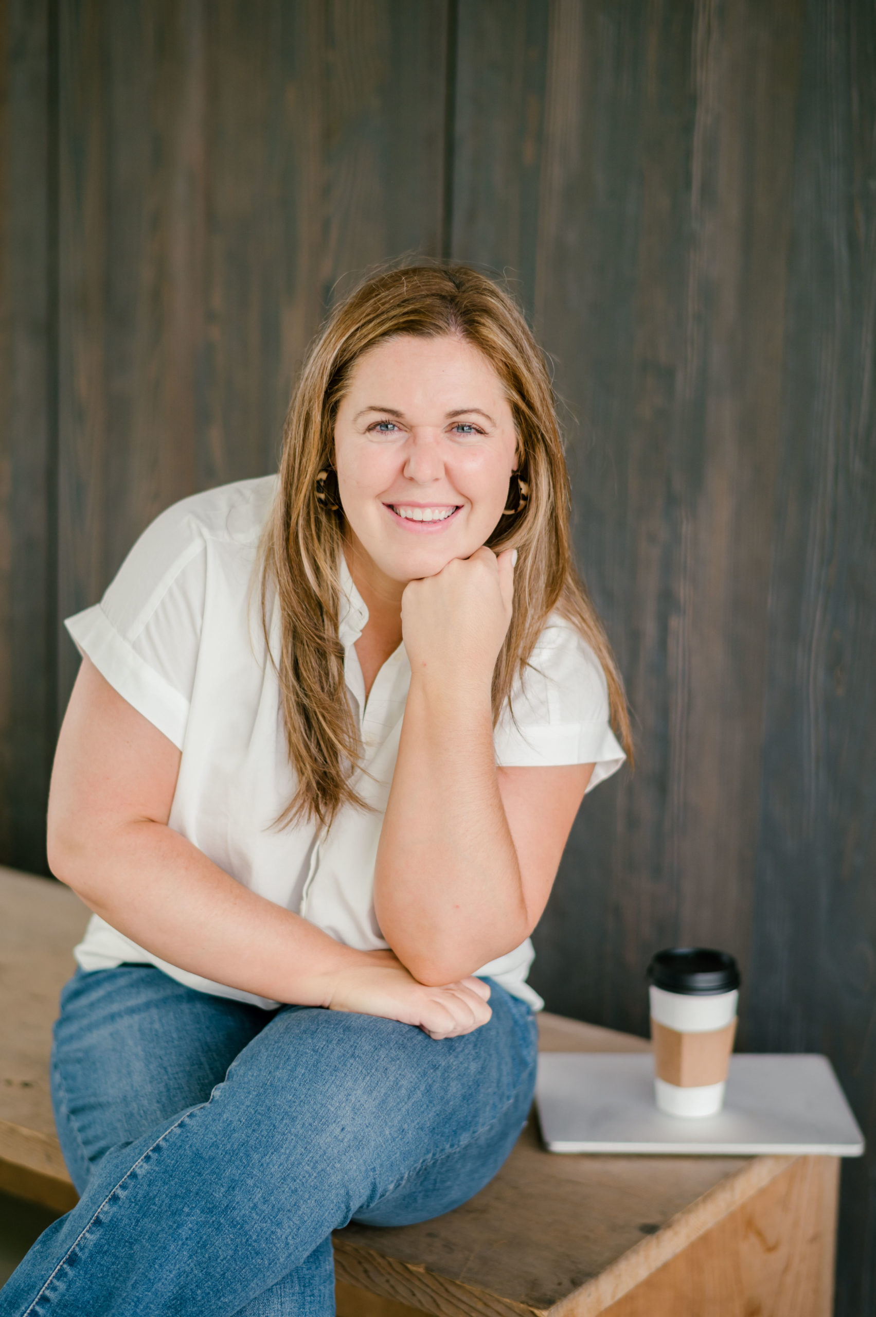 Woman sitting on a wooden bench smiling with a laptop and coffee sitting on the bench her personal brand photos