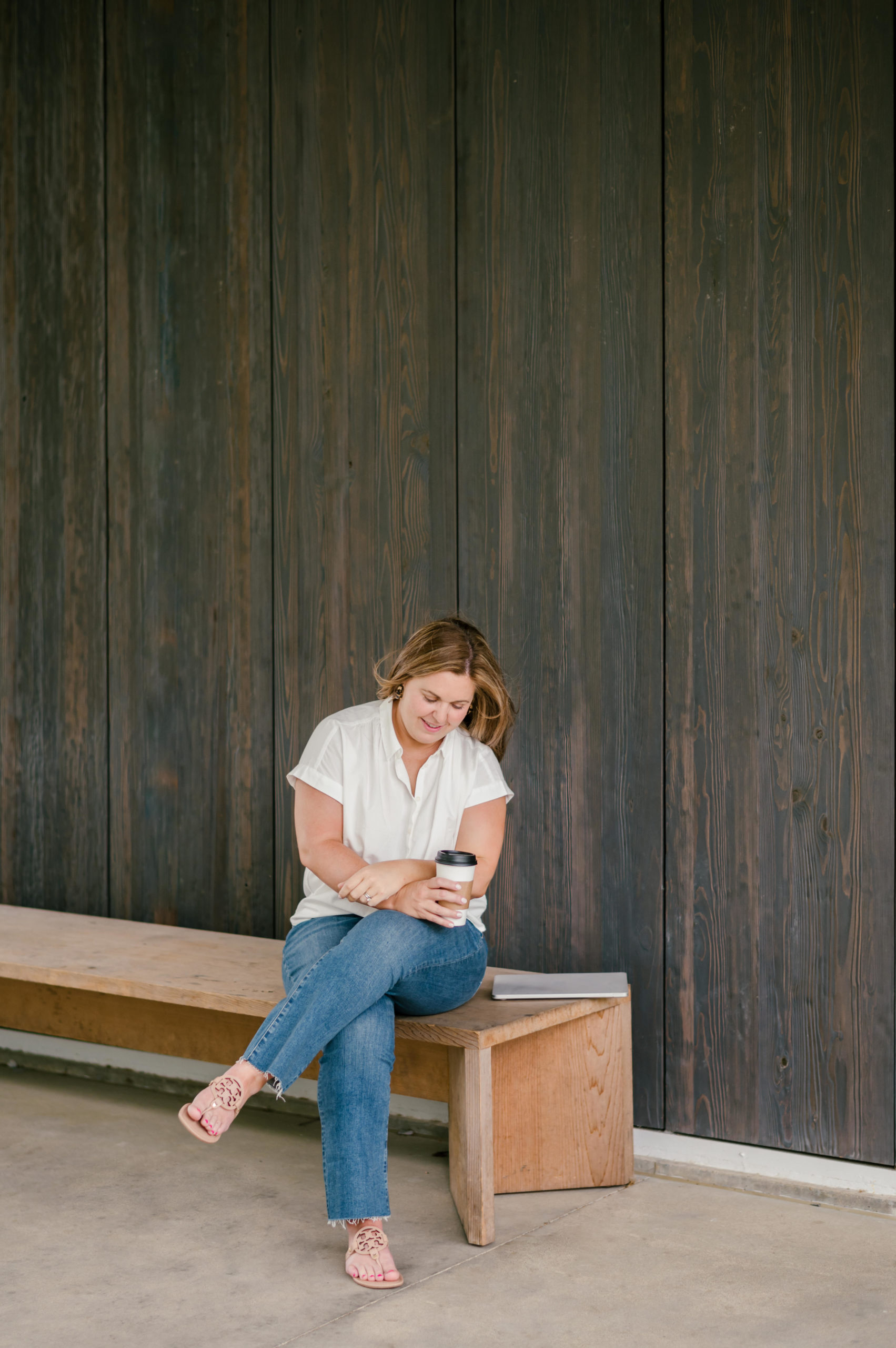 Woman sitting on a wooden bench holding a cup of coffee smiling