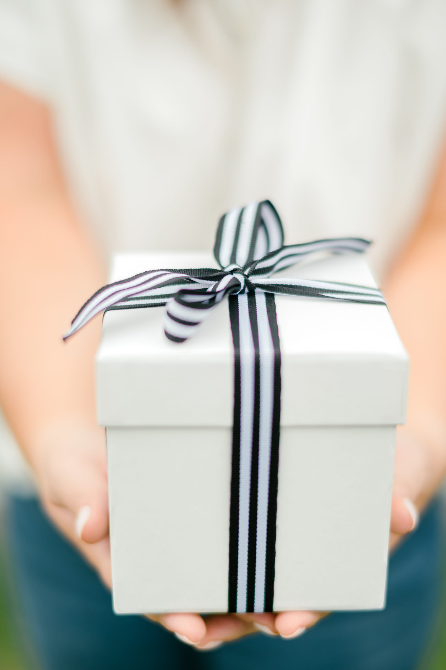 Woman holding a white gift box wrapped in a striped blue and white ribbon