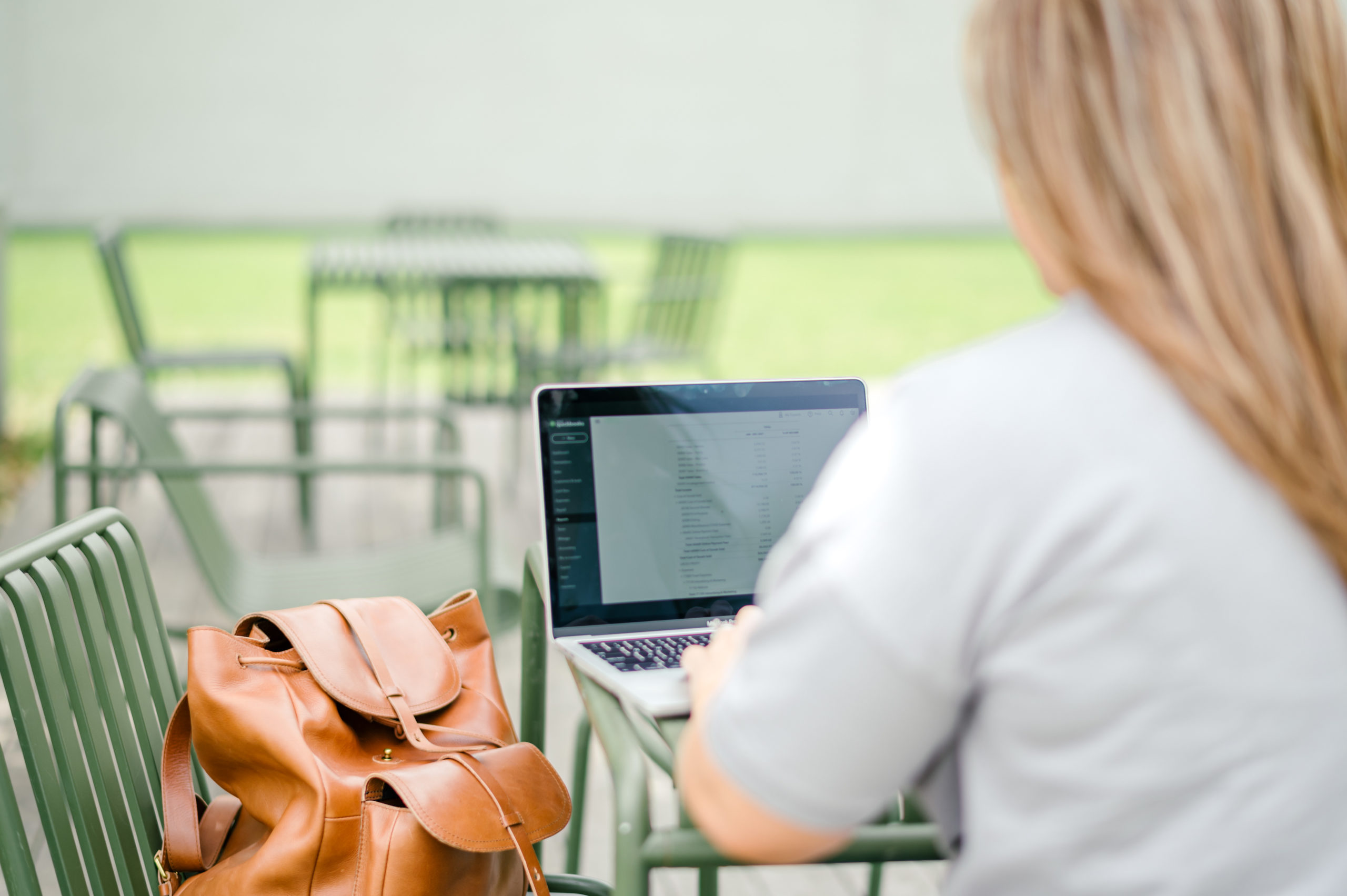 Woman working on computer laptop on a green table outside