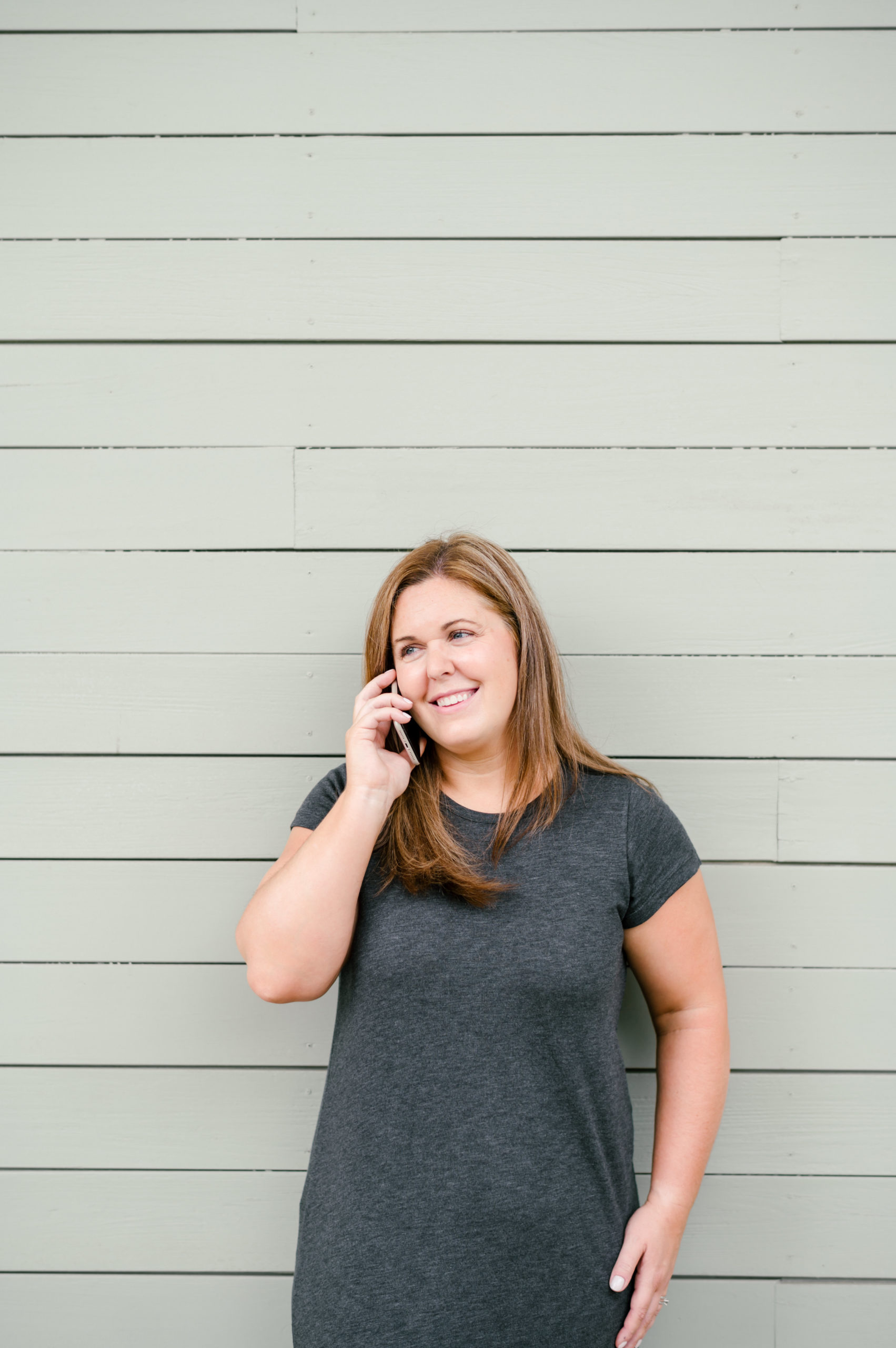 Woman smiling talking on her cellphone in a gray t-shirt dress