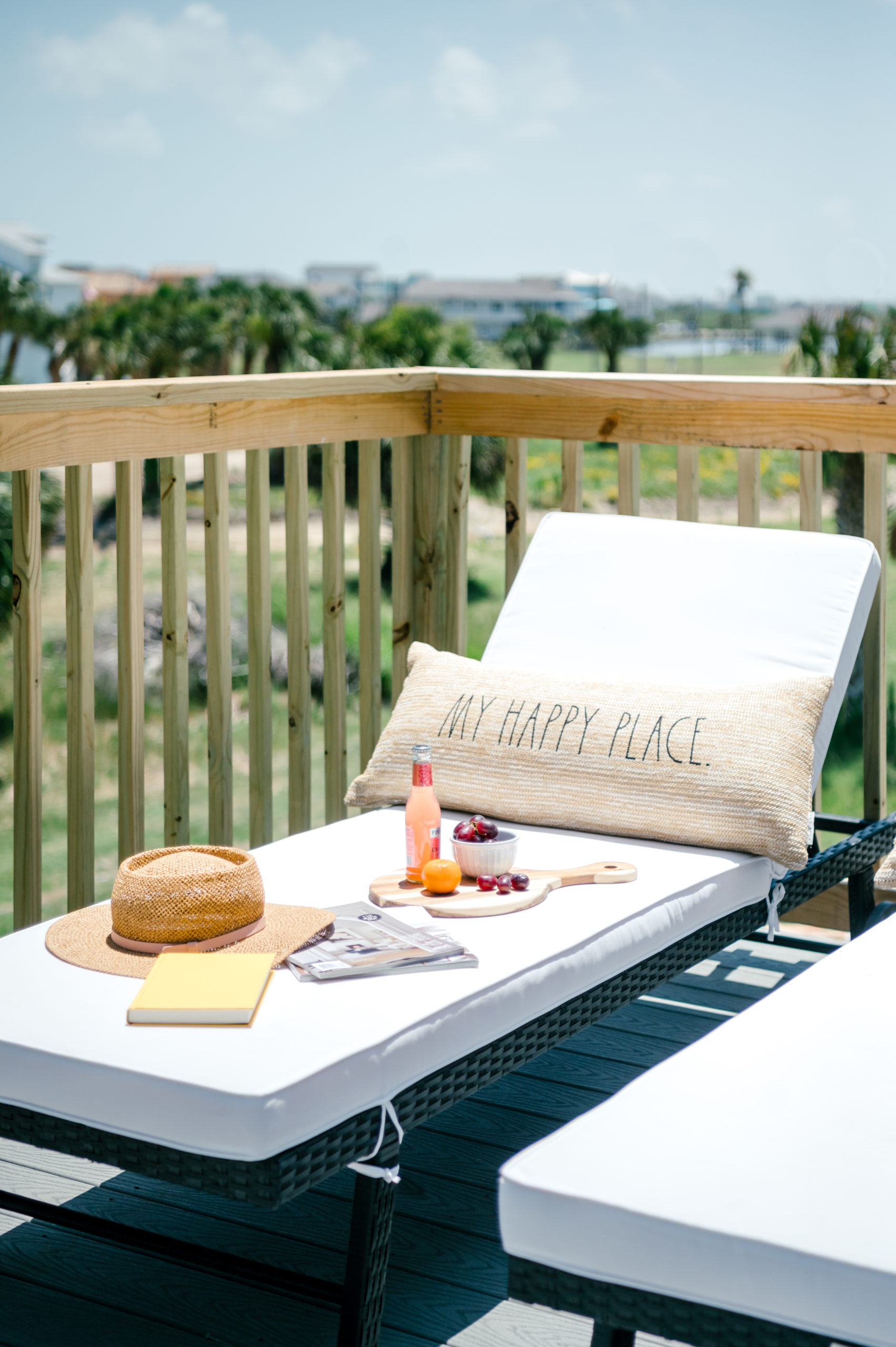 Outdoor lounge chairs with tan pillows reading "Happy place" sitting on the balcony