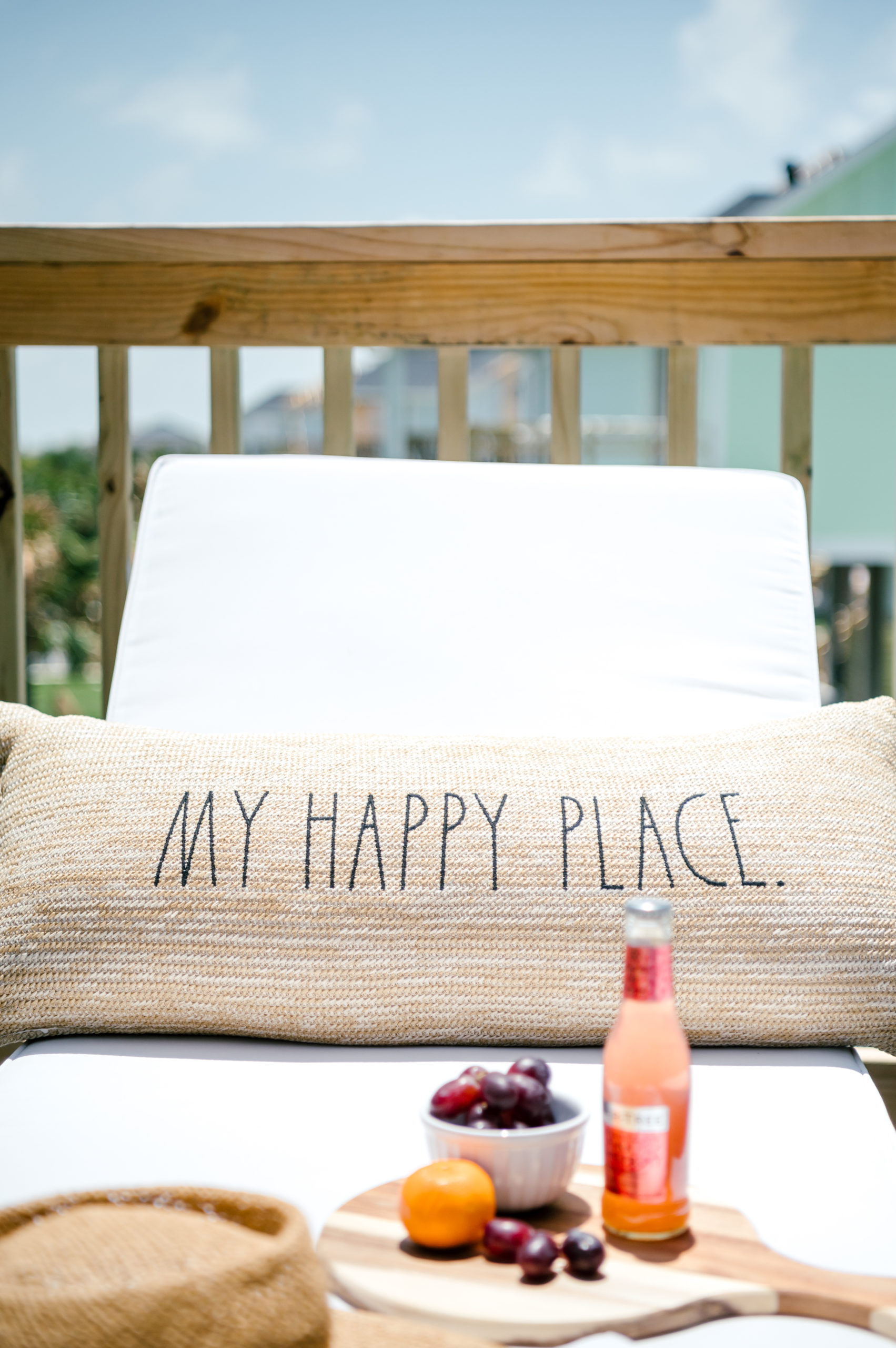 Outdoor lounge chairs with tan pillows reading "Happy place" sitting on the balcony