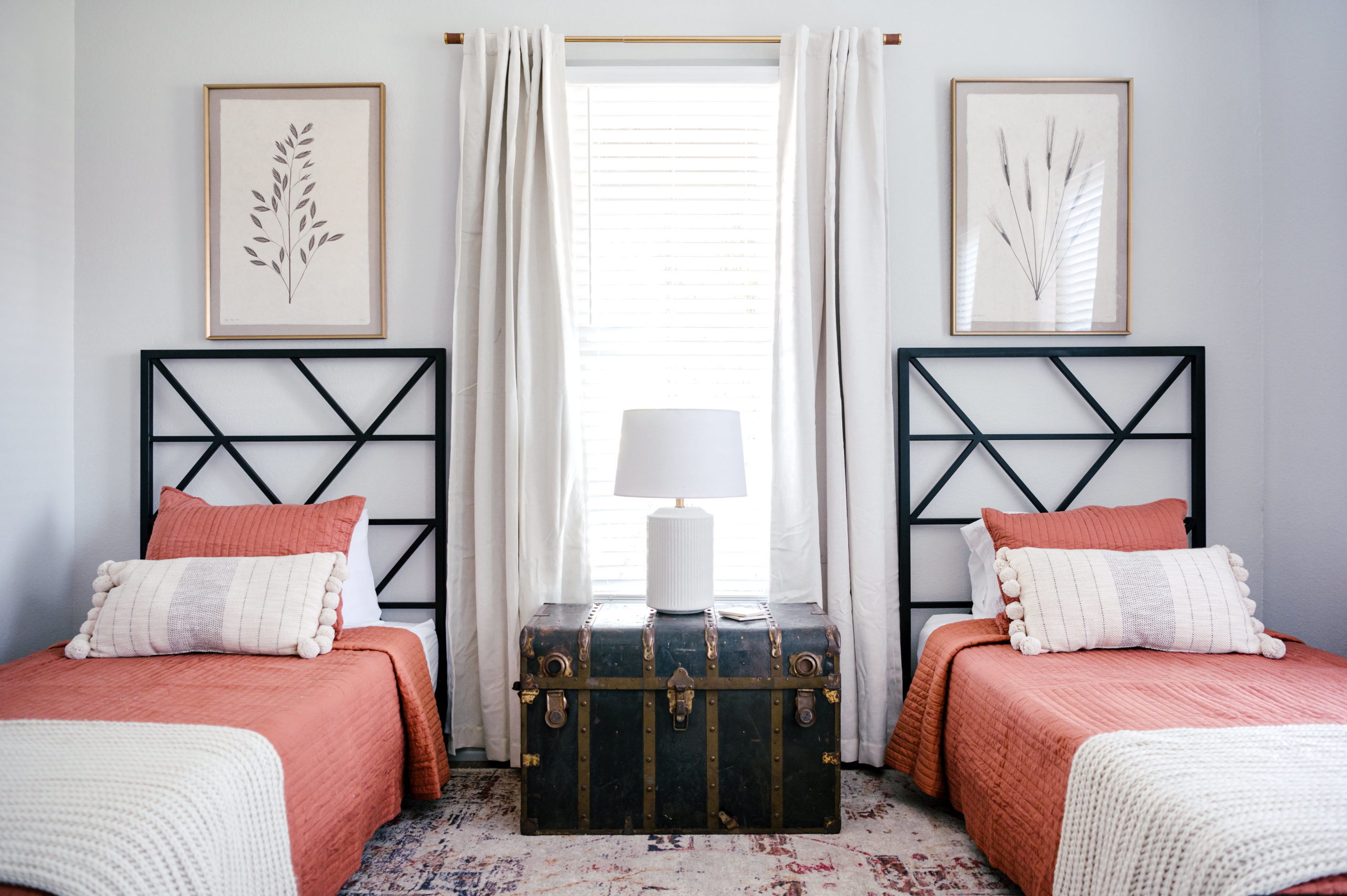 Twin sized beds with red bed comforters and white pillows next to a black cedar chest