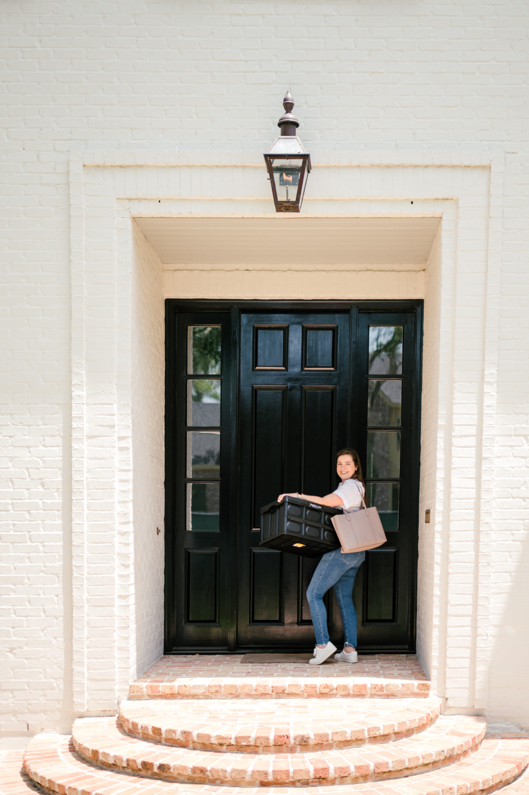Woman standing holding a black box walking into the door of the front house 