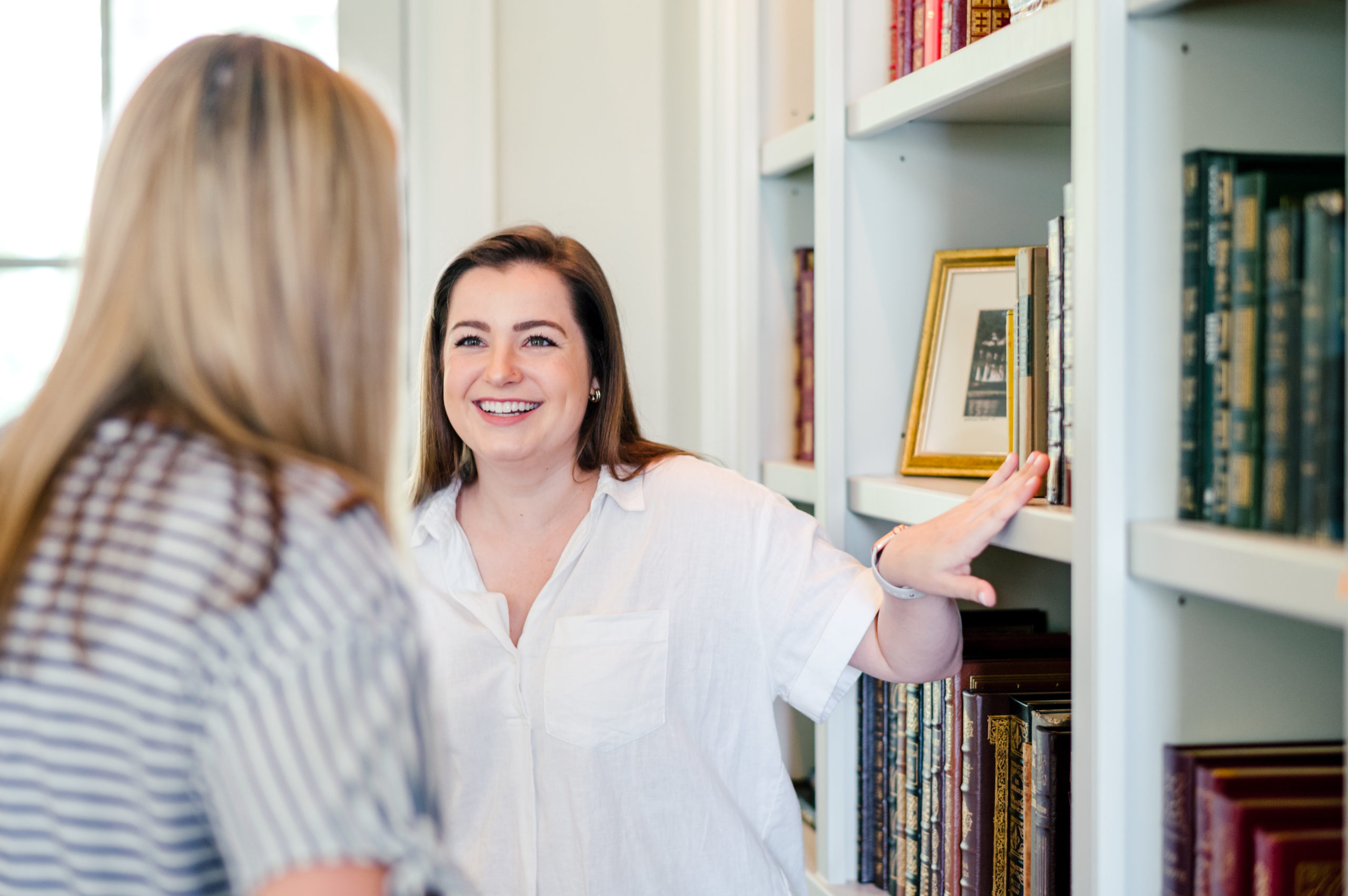 Woman smiling at client while pointing at book shelf