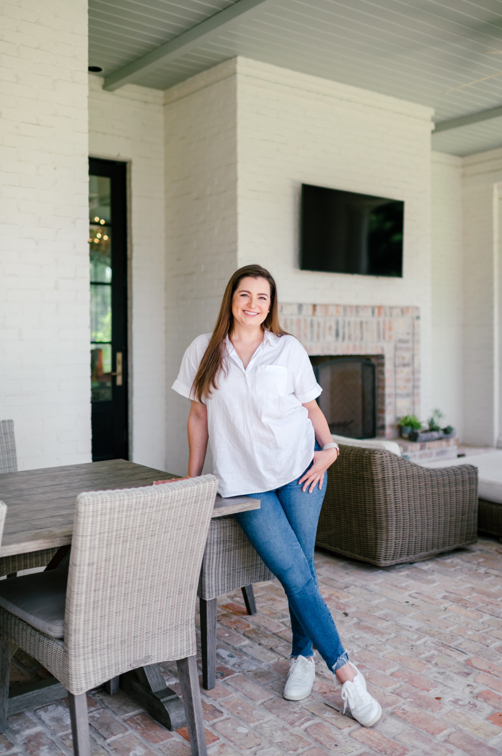 Photo of a Woman standing on the patio and smiling in blue jeans and a white shirt Houston Brand Photographer