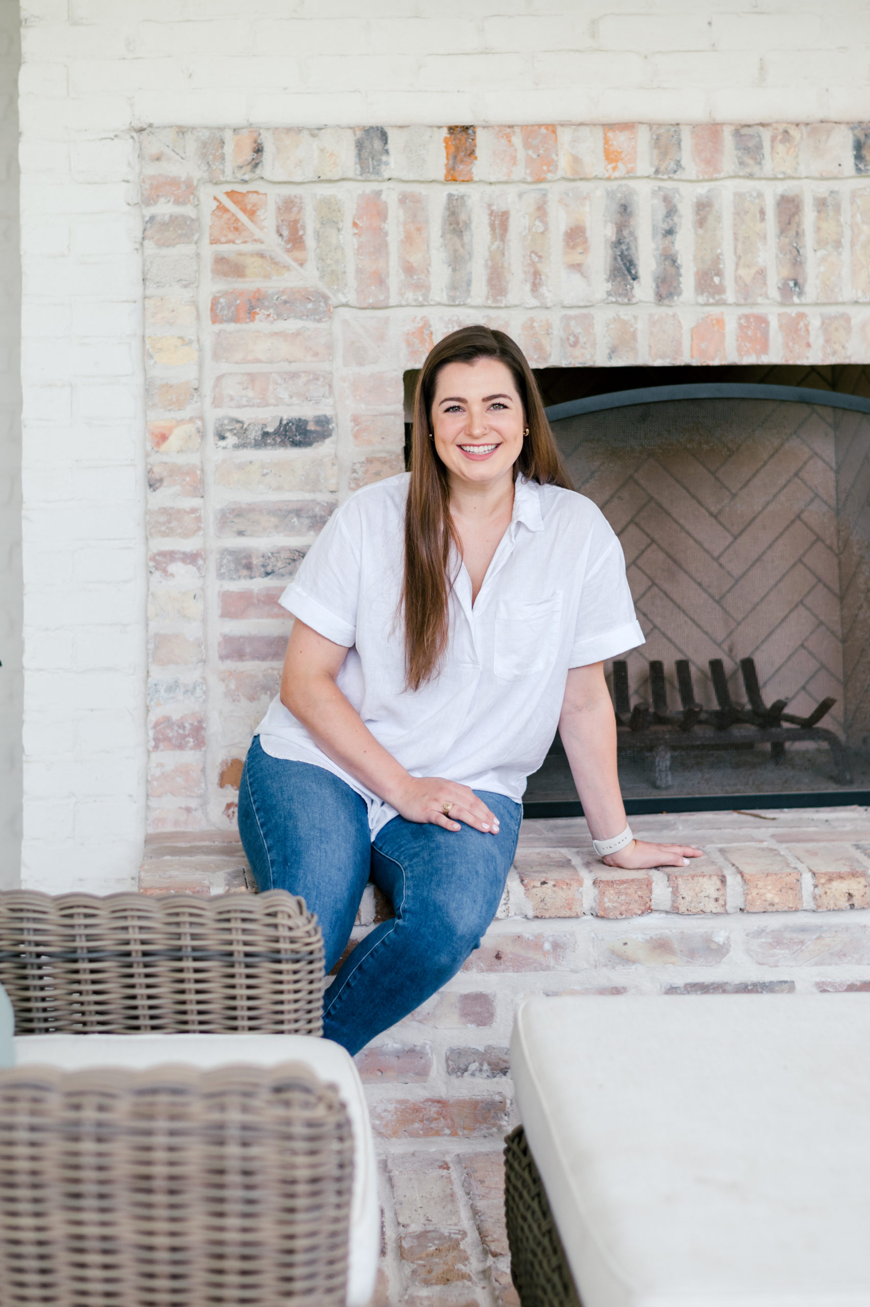 Photo of a Woman sitting on fireplace ledge smiling in blue jeans and a white shirt Houston Brand Photographer