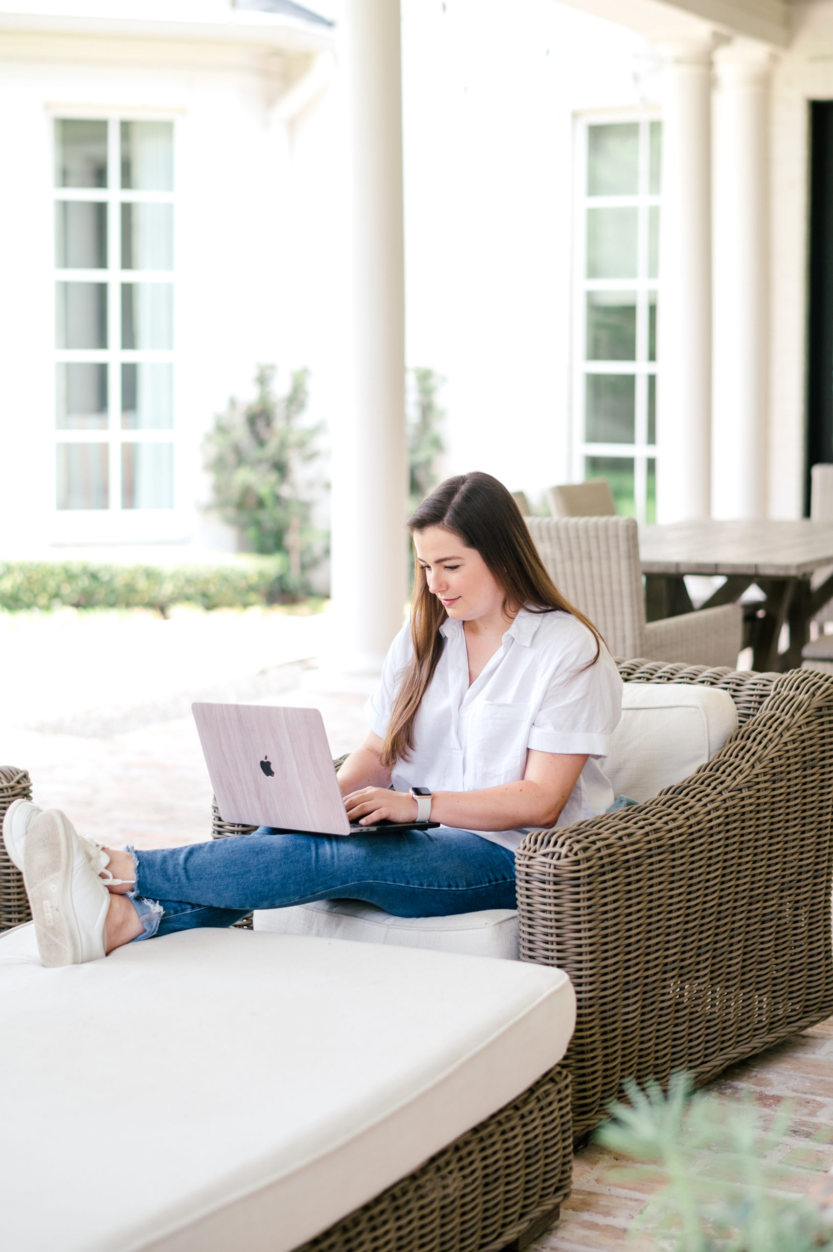 Woman sitting on patio furniture working on laptop