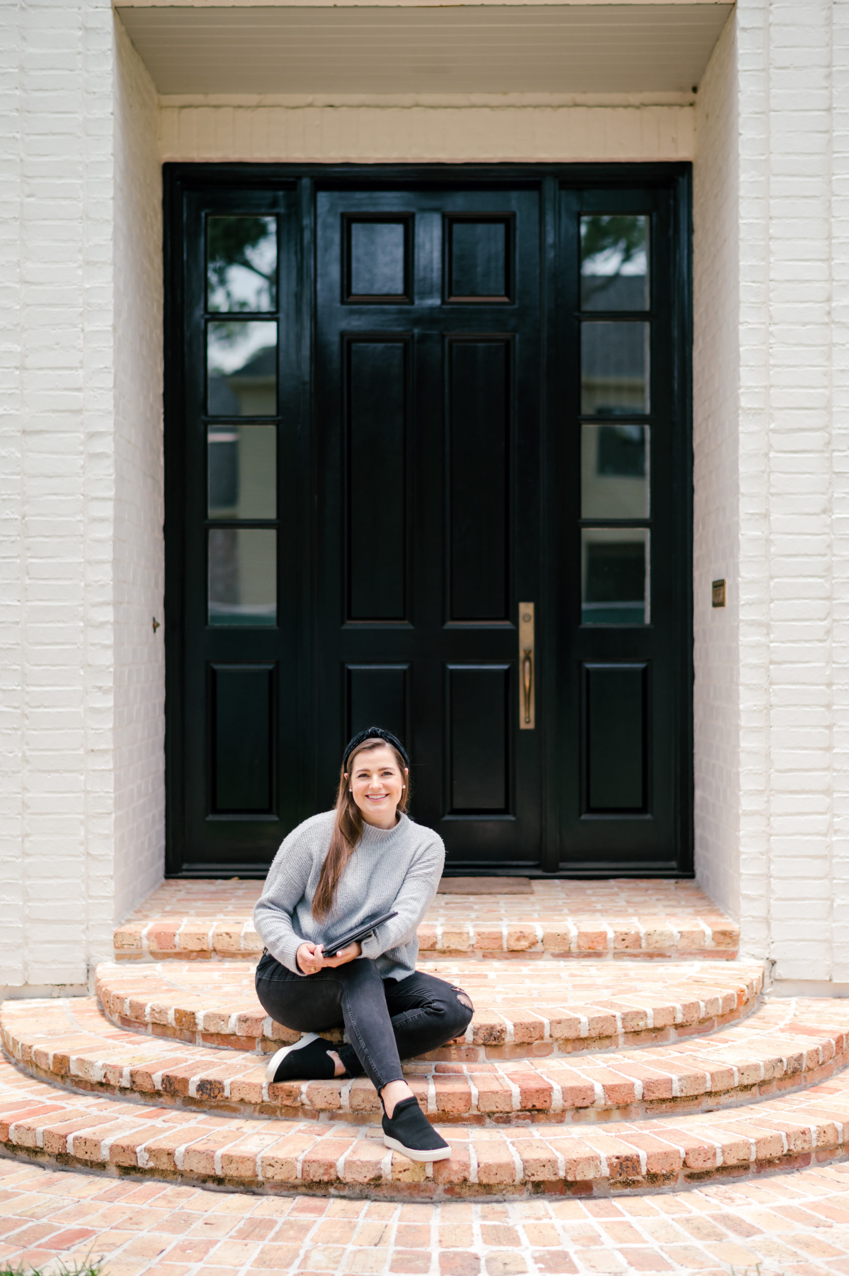 Woman sitting on front door steps in dark jeans and grey sweater