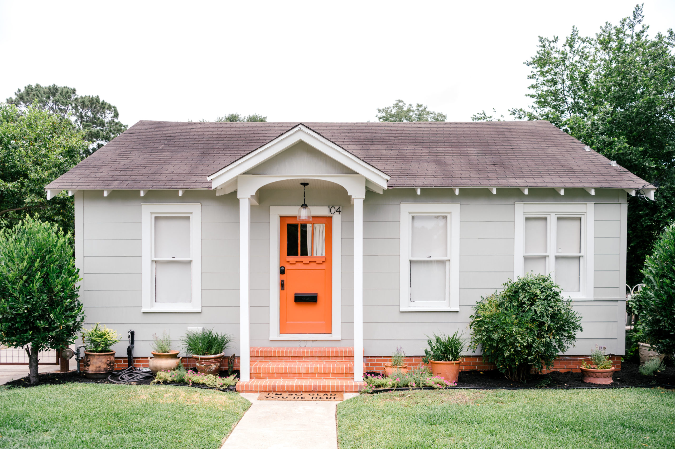 Short-term Rental Photos of the exterior of a grey one story home with an orange door and steps