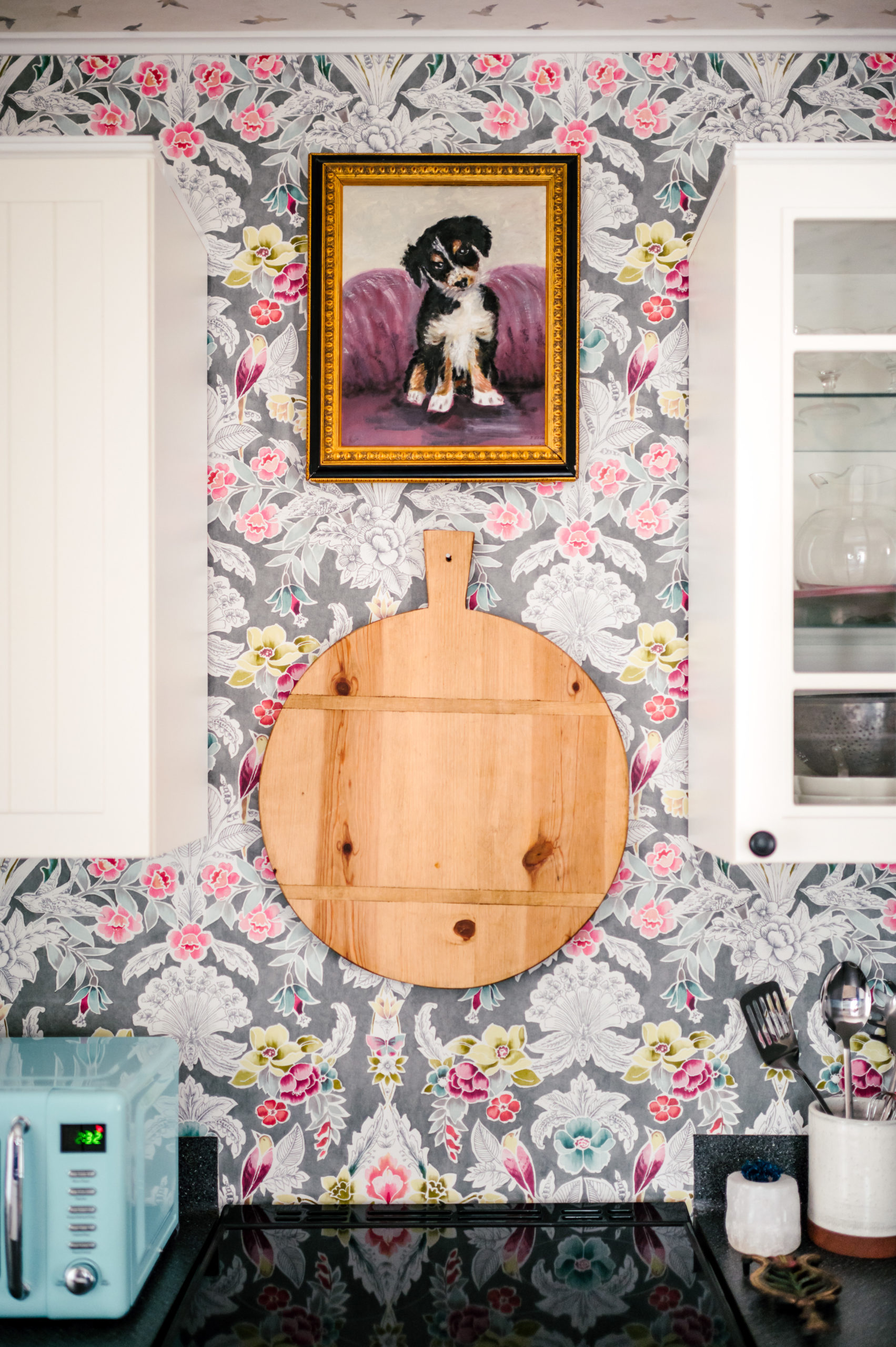 Short-term Rental Photos of kitchen wall with colorful floral wallpaper and cutting board hanging underneath a frame of a puppy