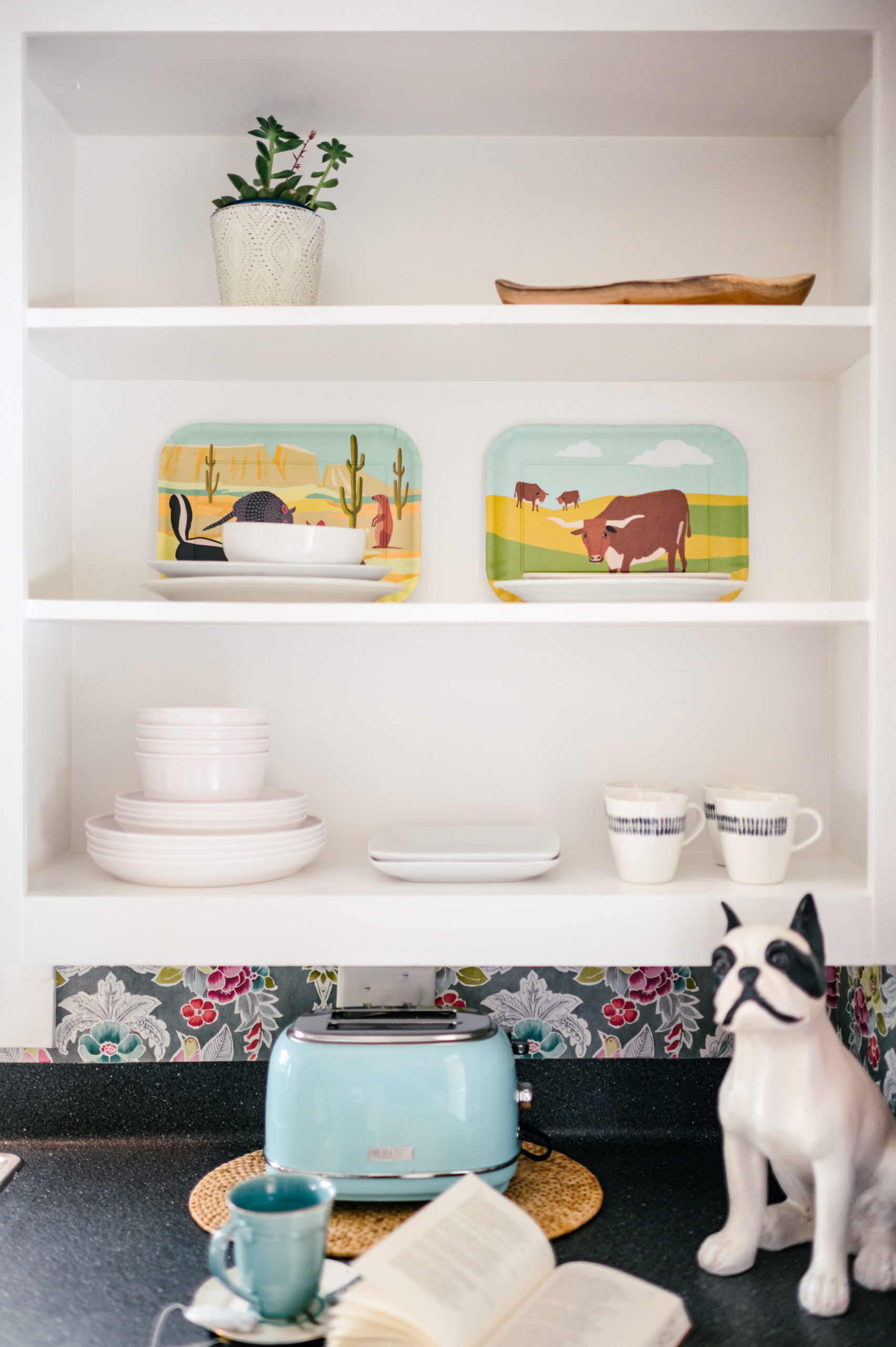 Kitchen shelving with dishware and countertop with a blue toaster and puppy figurine