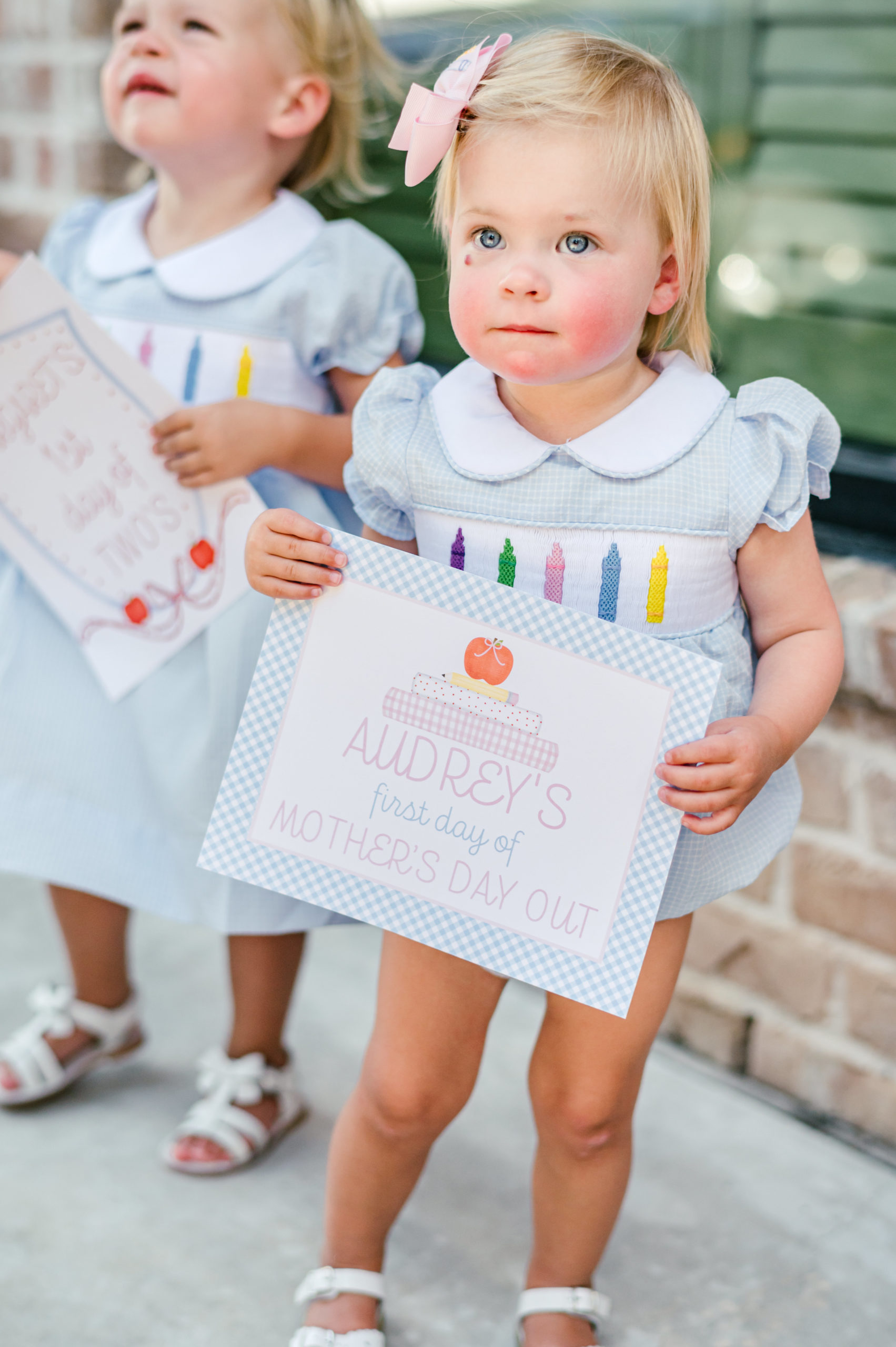 Little girl holding a milestone card labeled "Audreys first day of mothers day out"