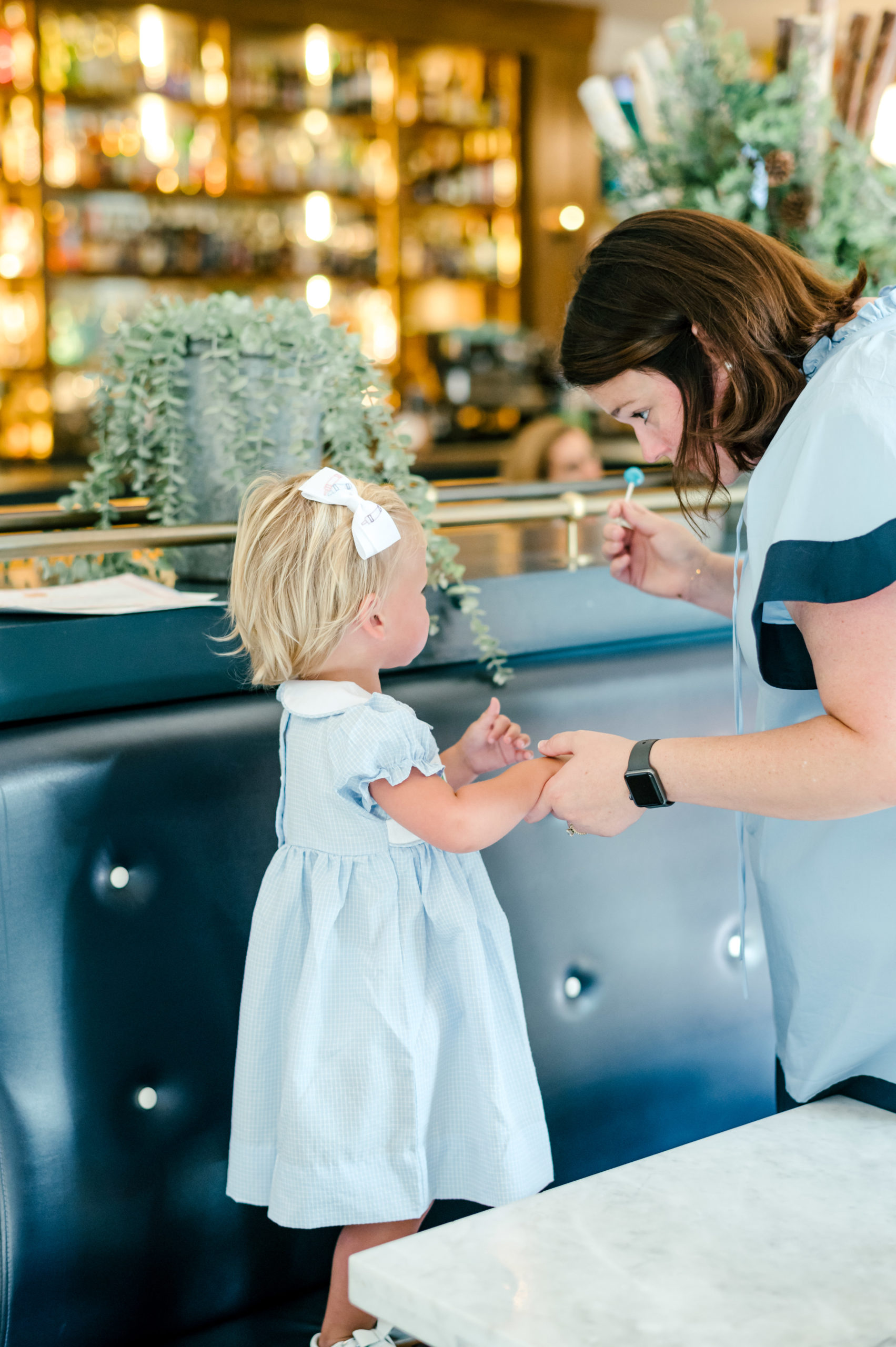 Woman giving a lollipop to little girl wearing a blue dress