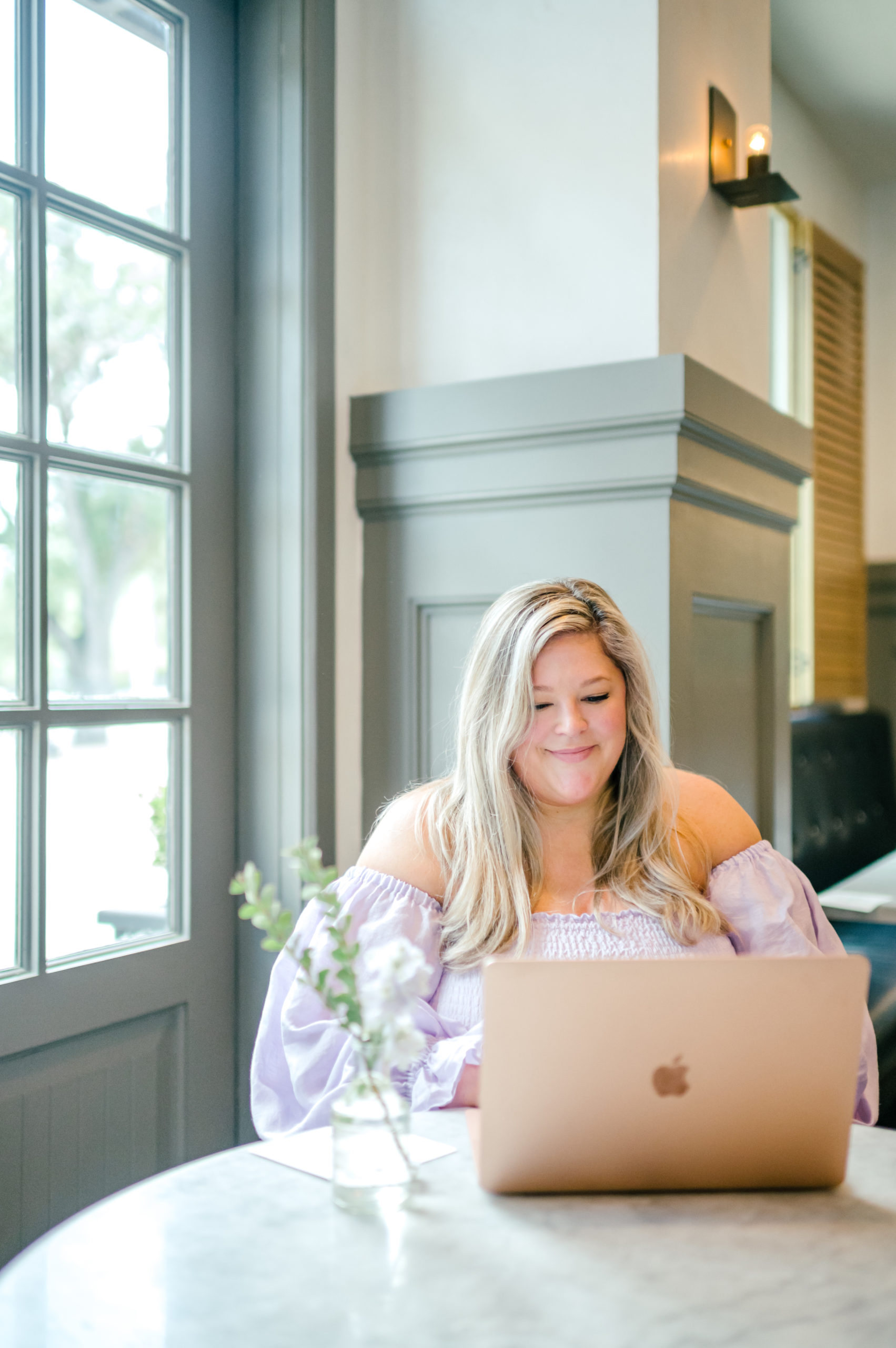 Woman sitting at the table typing on apple computer posing for for brand photoshoot