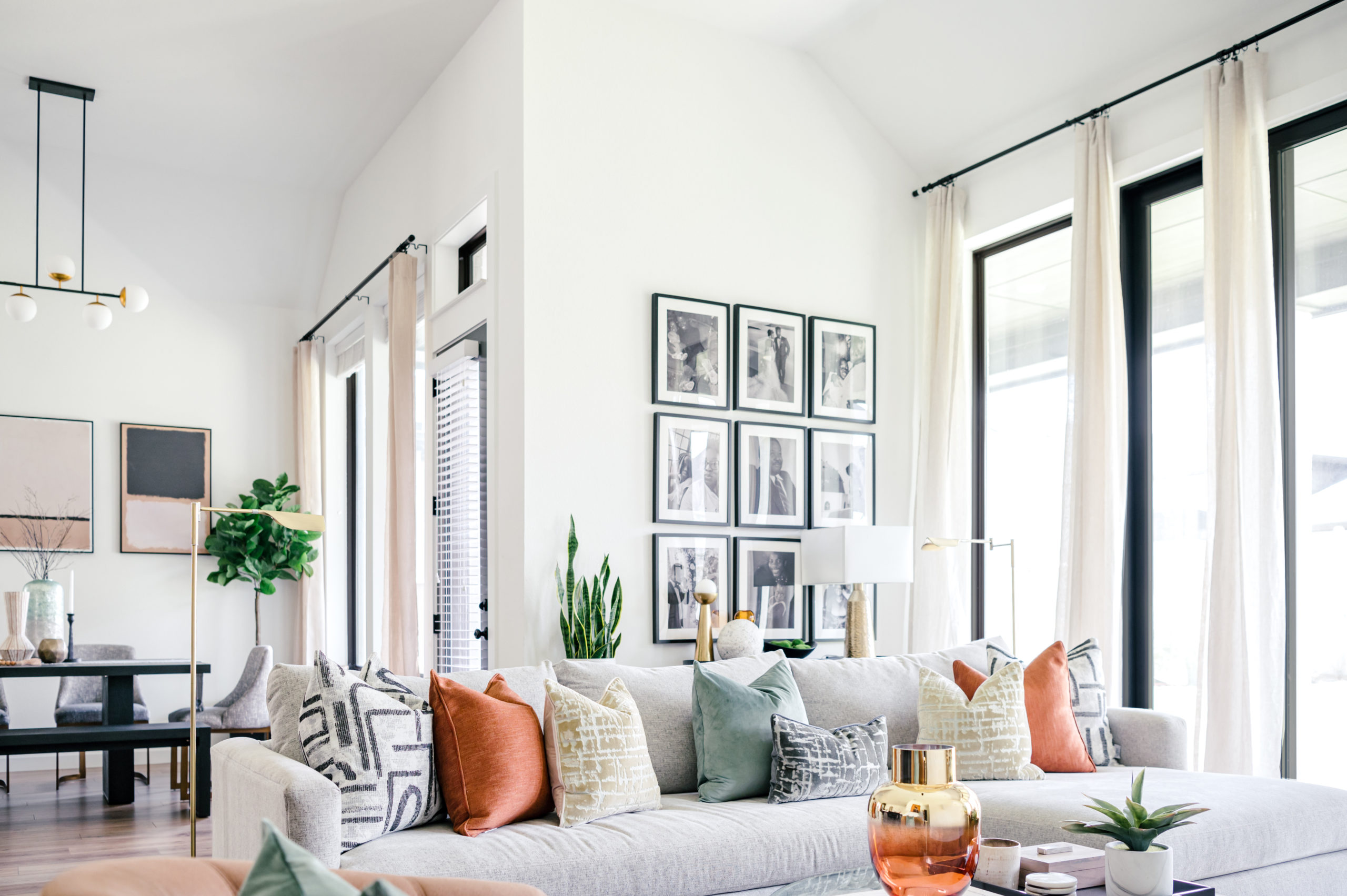 Living room interior design, light grey couch with blue, white, and orange pillows, in front of a wall with family photos hanging