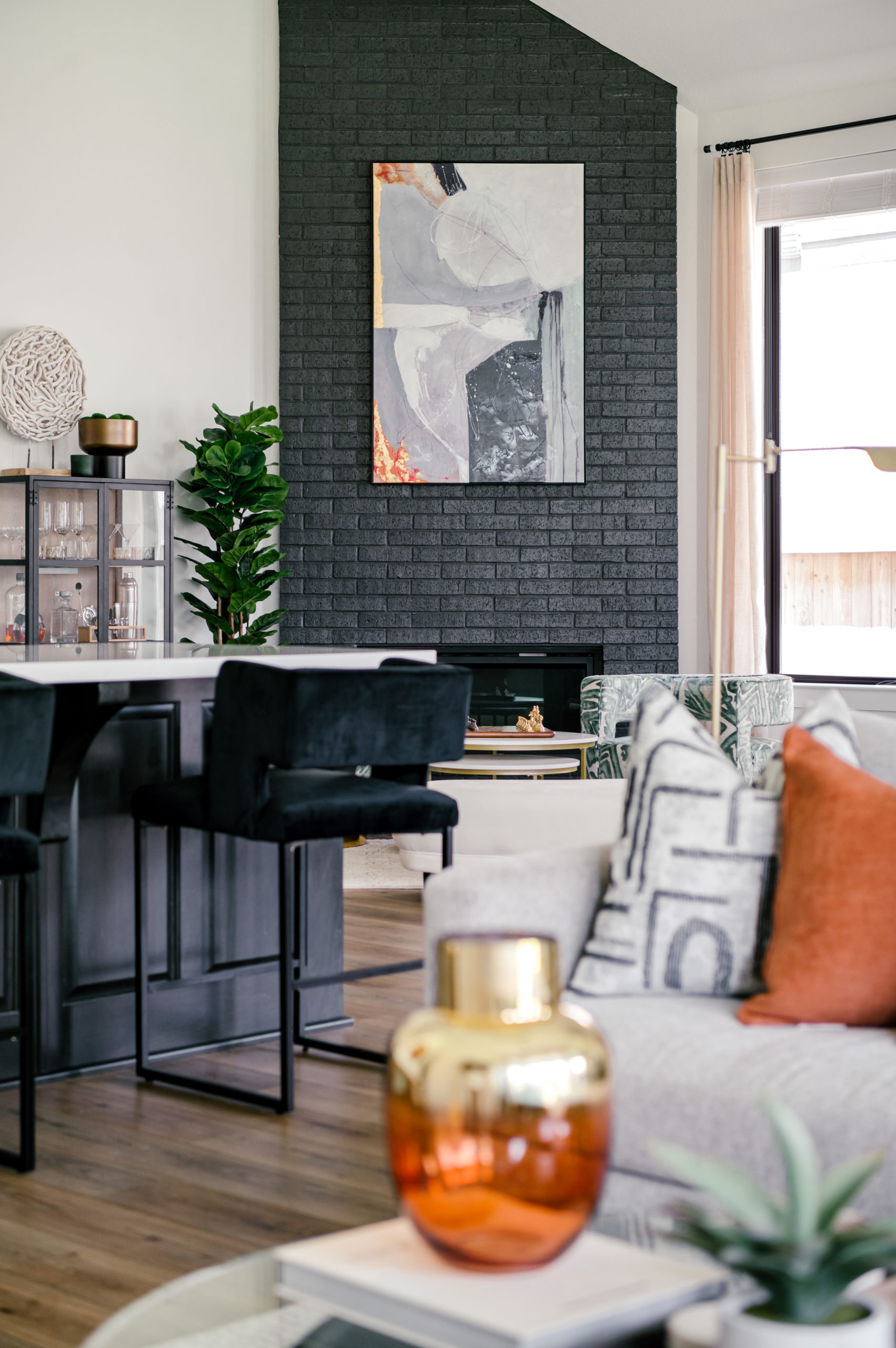 Living room and kitchen interior design, black bar stool sitting on the edge of the kitchen island, wall art on black brick wall hanging above fireplace
