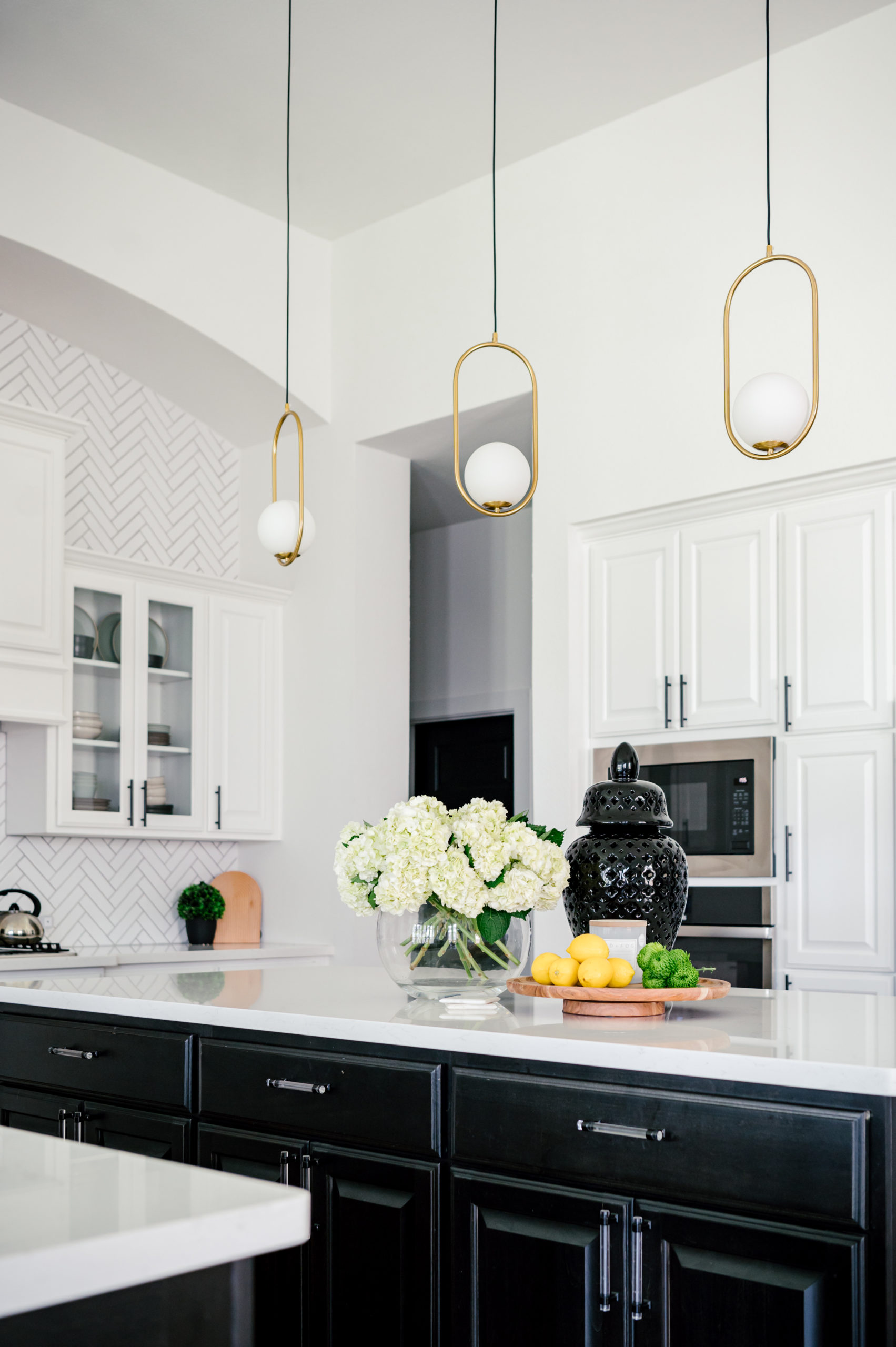 Black kitchen cabinets and black island and white florals sitting on top of the marble kitchen counter