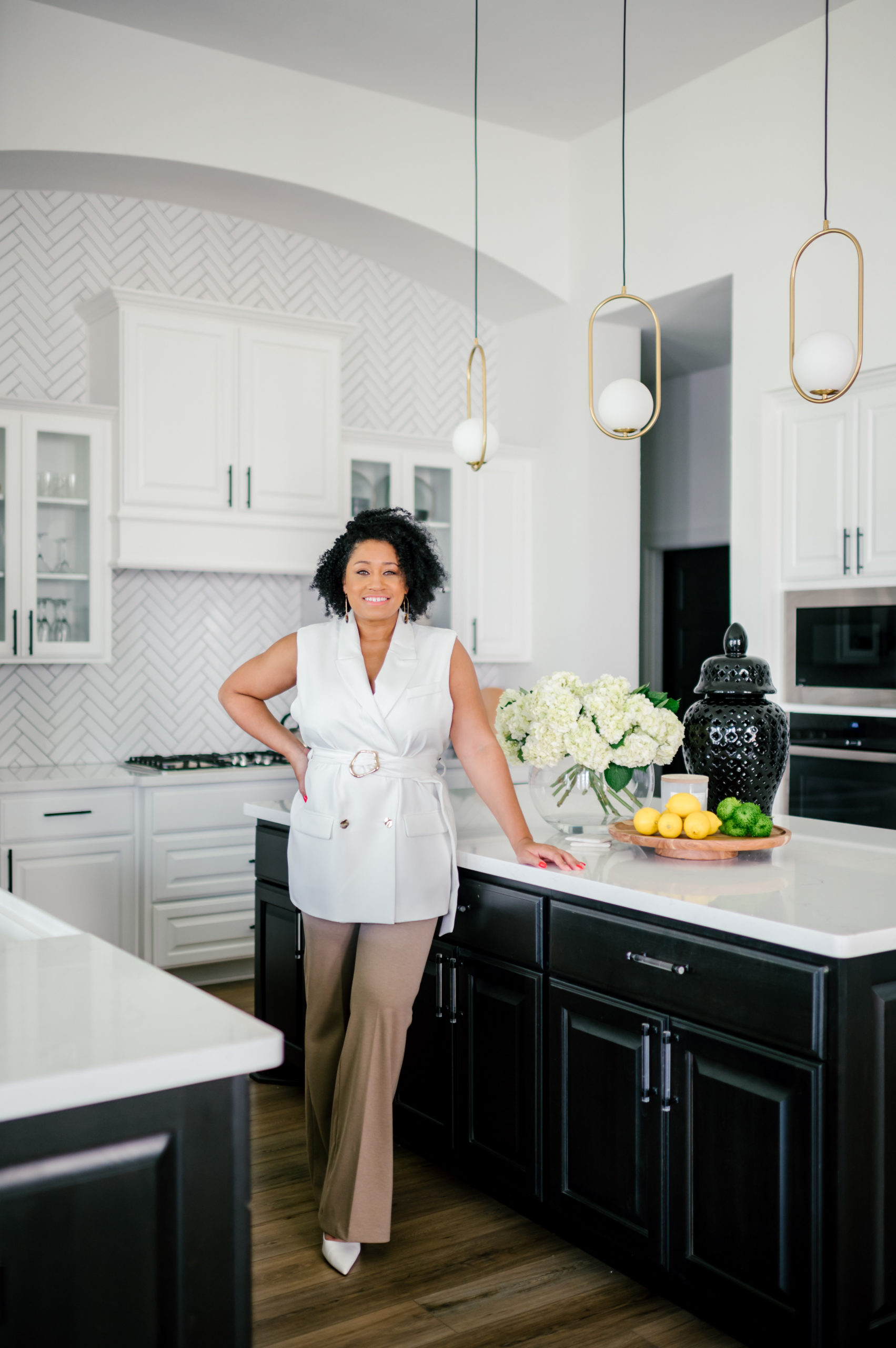 Professional interior photography of interior designer standing in a white blouse and khaki pants leaning on marble kitchen counter smiling
