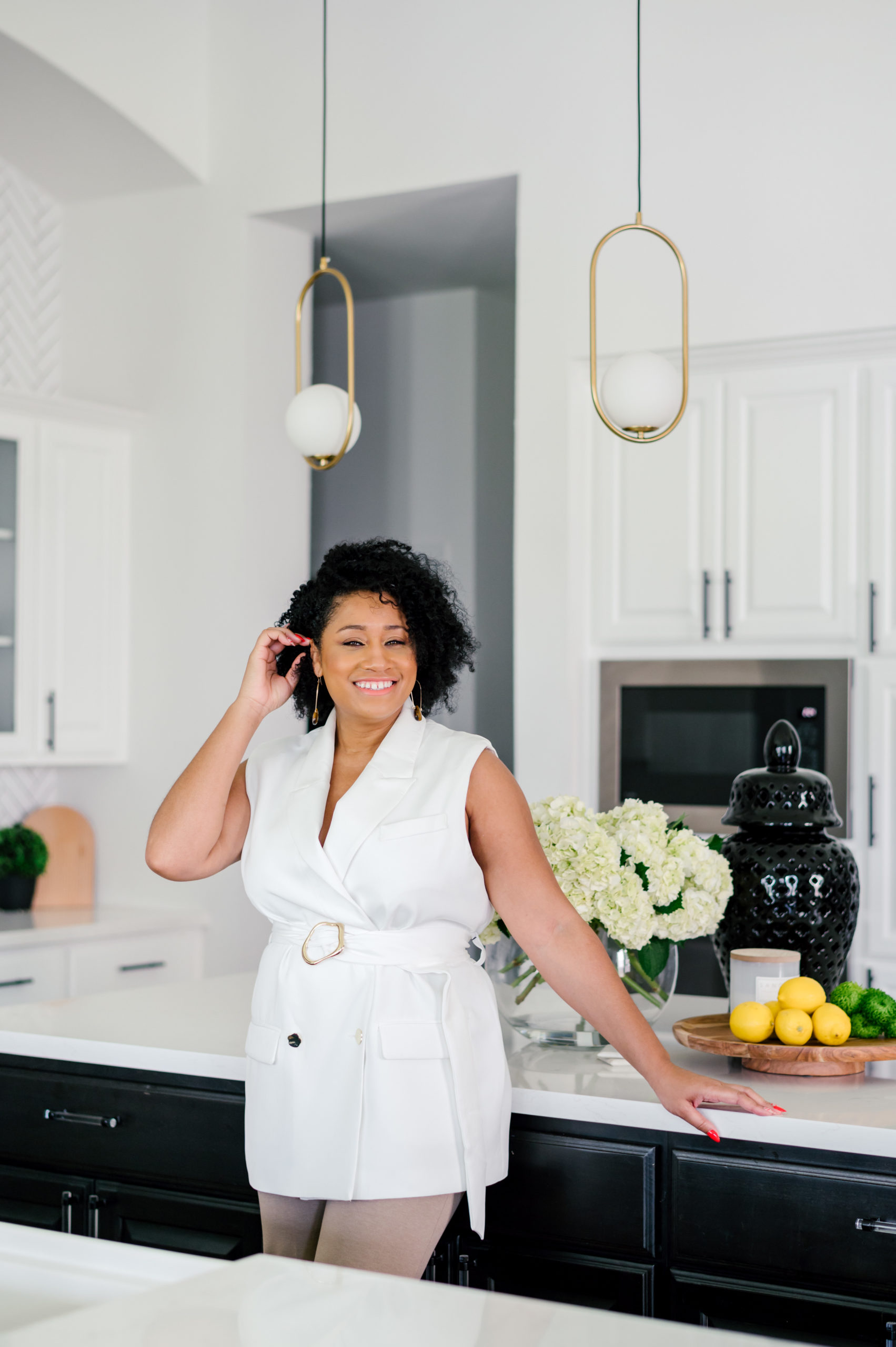 Professional interior photography of interior designer standing in a white blouse and khaki pants leaning on marble kitchen counter smiling