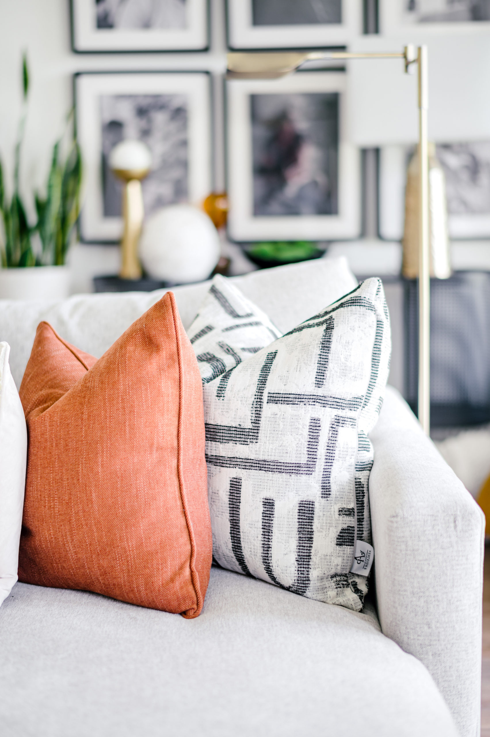 Orange and white and black designed pillow sitting on a light grey colored couch